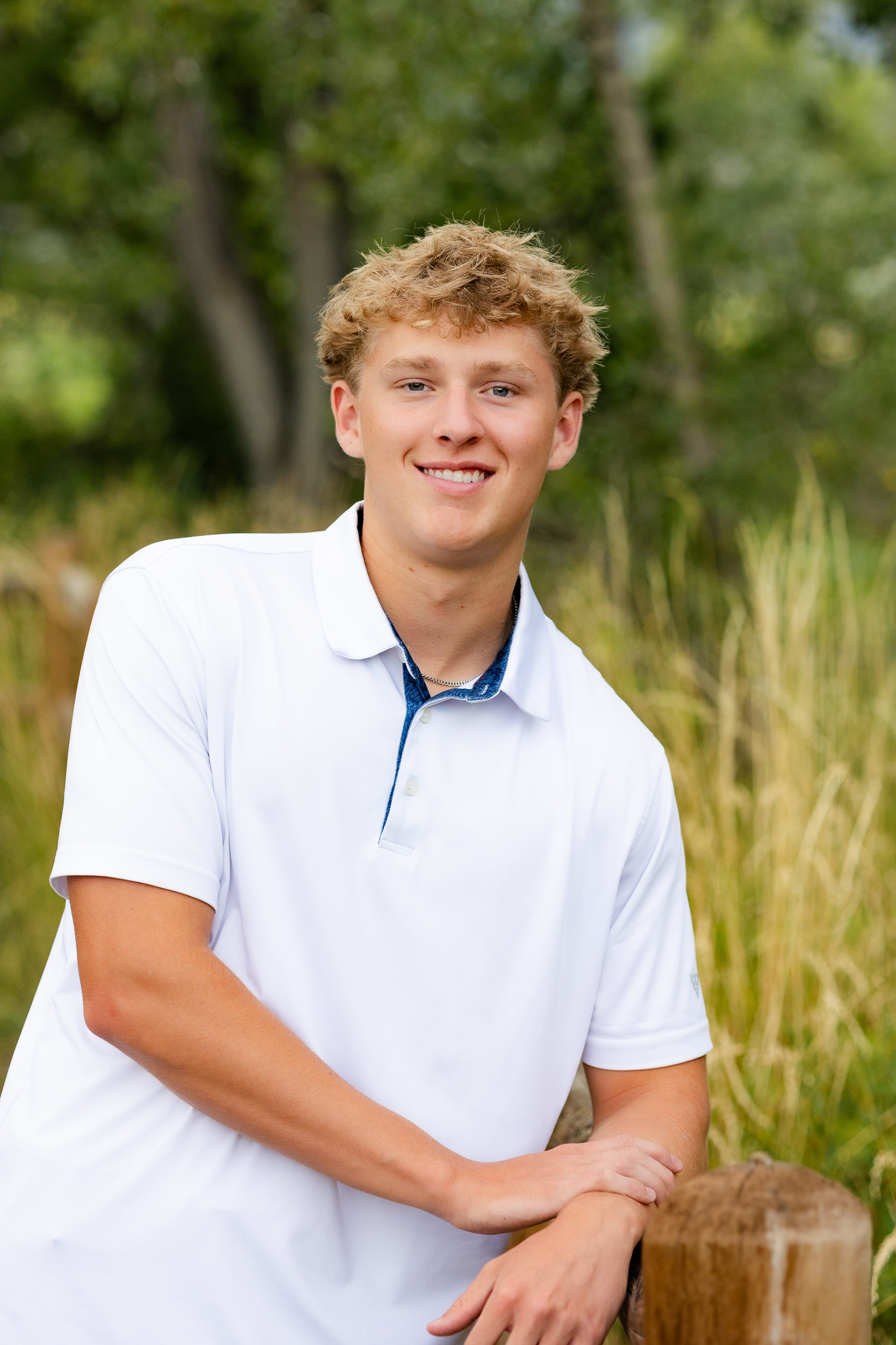 A young man leans on a trailside fence and smiles at the camera.