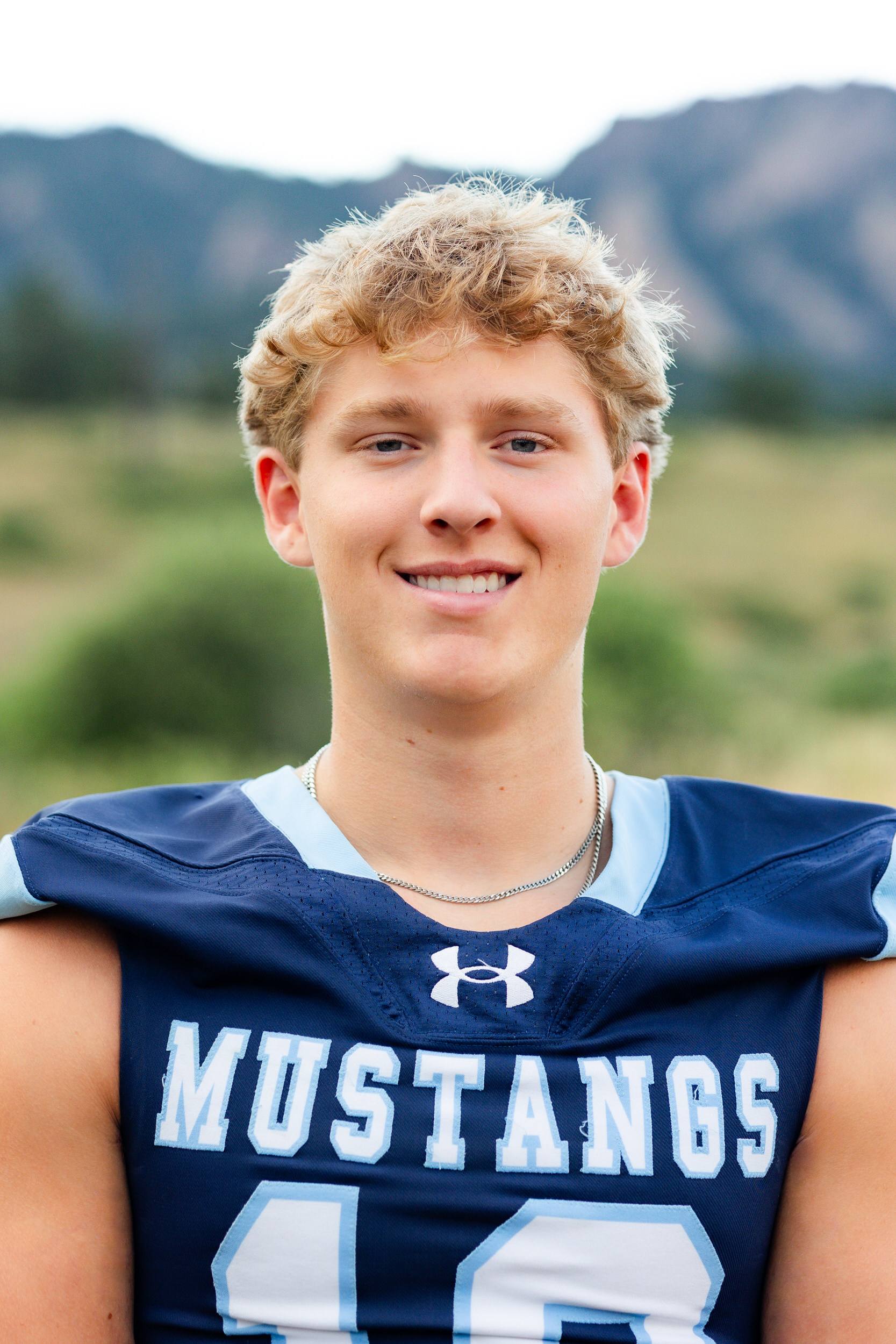 A young man in a school football jersey smiles at the camera.