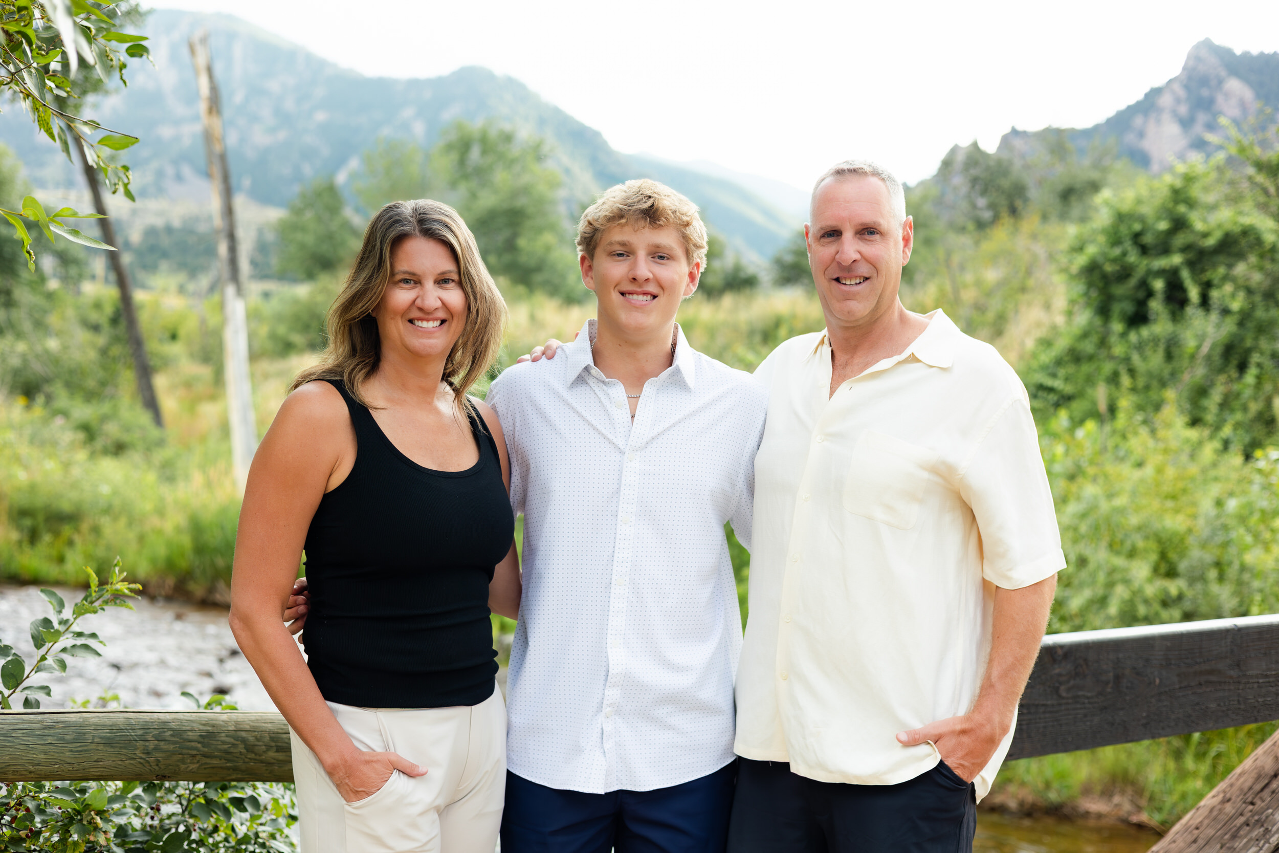 Parents stand with their high school senior son between them and smile at the camera.