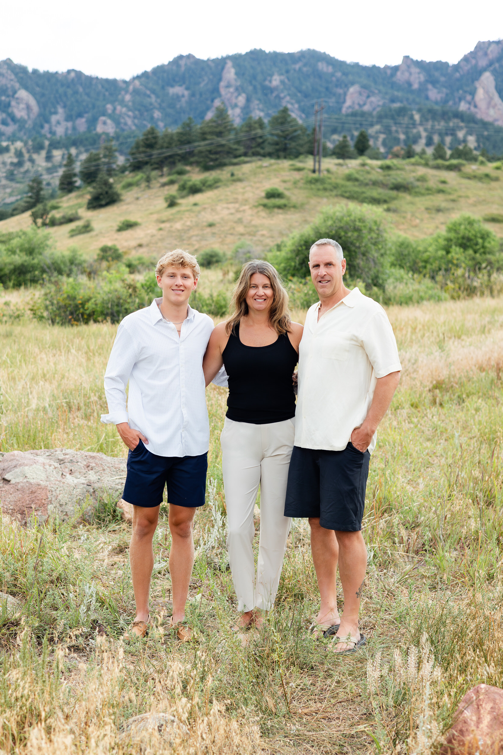 Family of three standing and smiling in a mountain field.