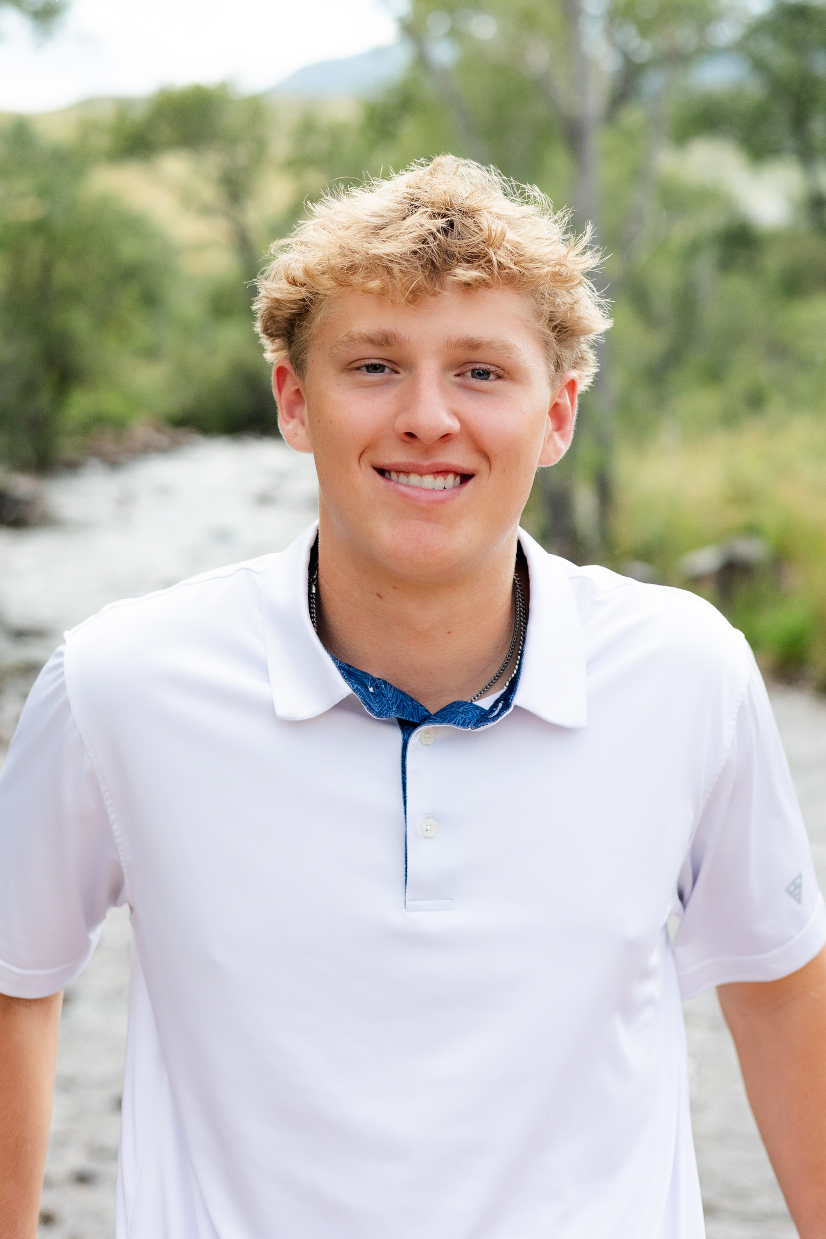 A young man standing on a bridge smiles at the camera.