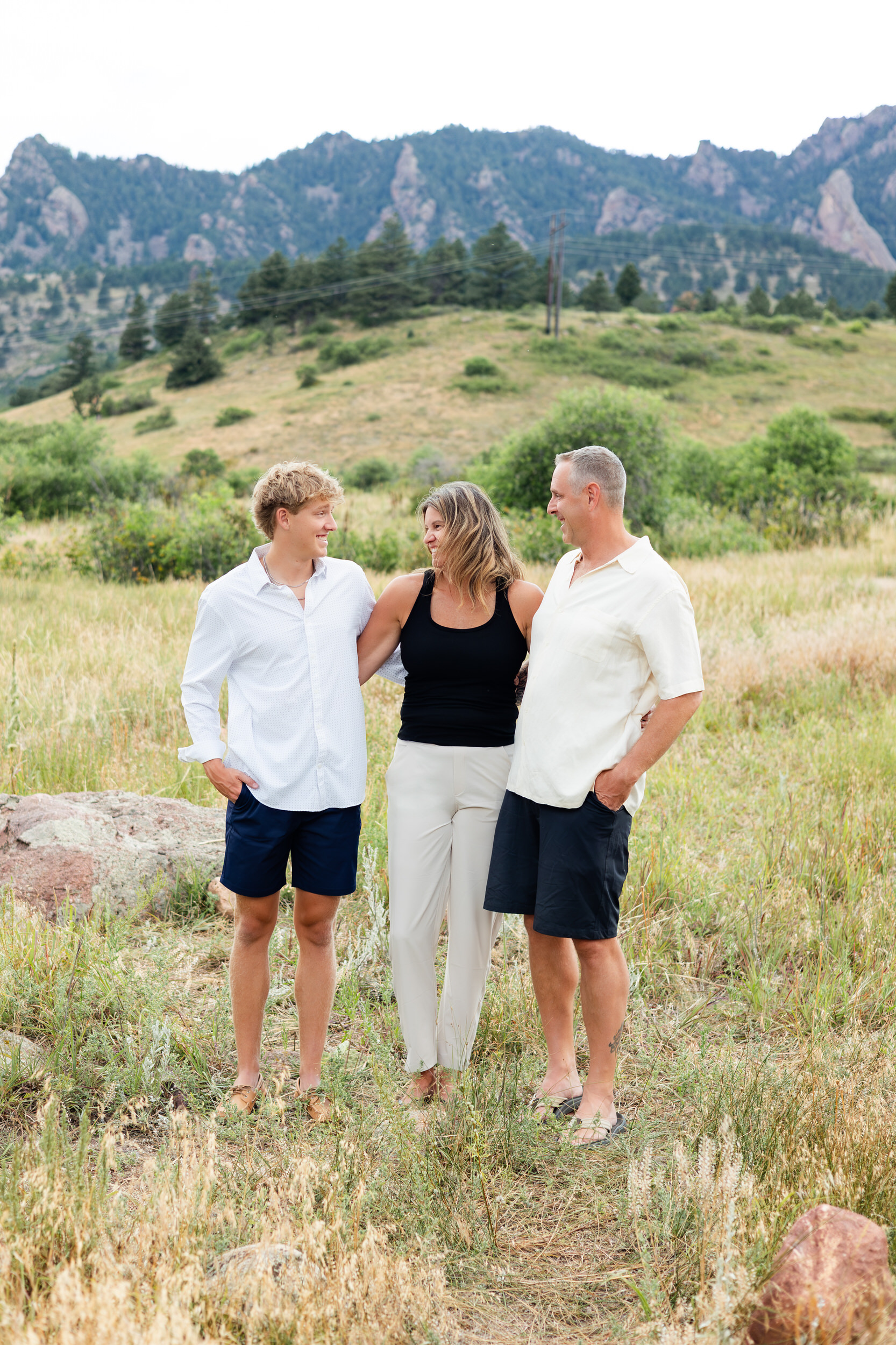 Family of three laughing with each other in a mountain field.