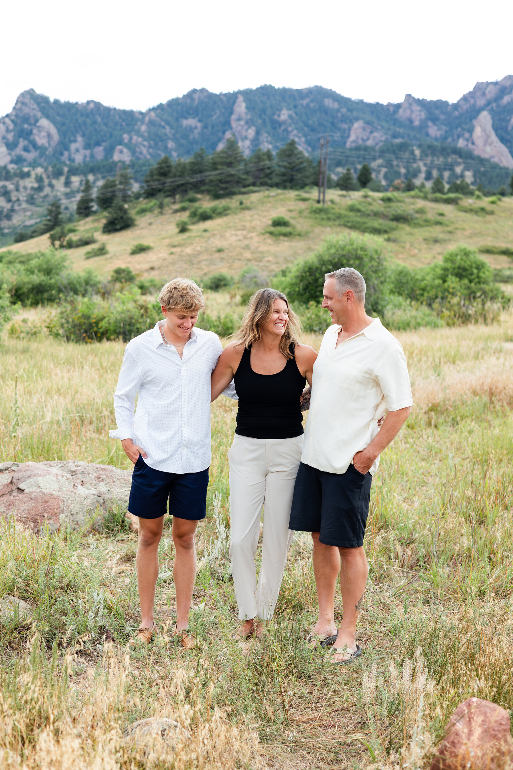 Family of three laughing with each other in a mountain field.