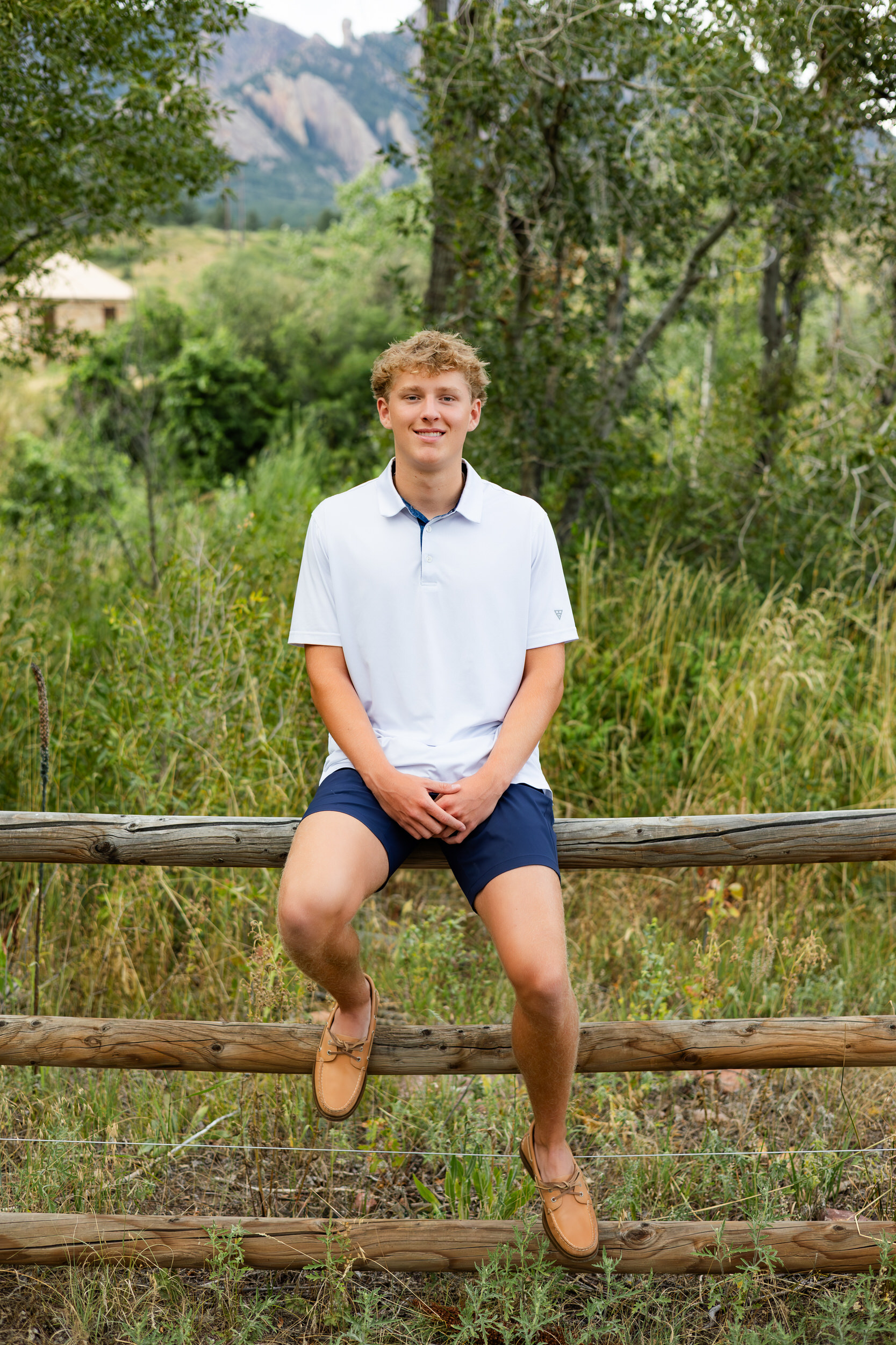 A young man sits on a trailside fence and smiles at the camera.