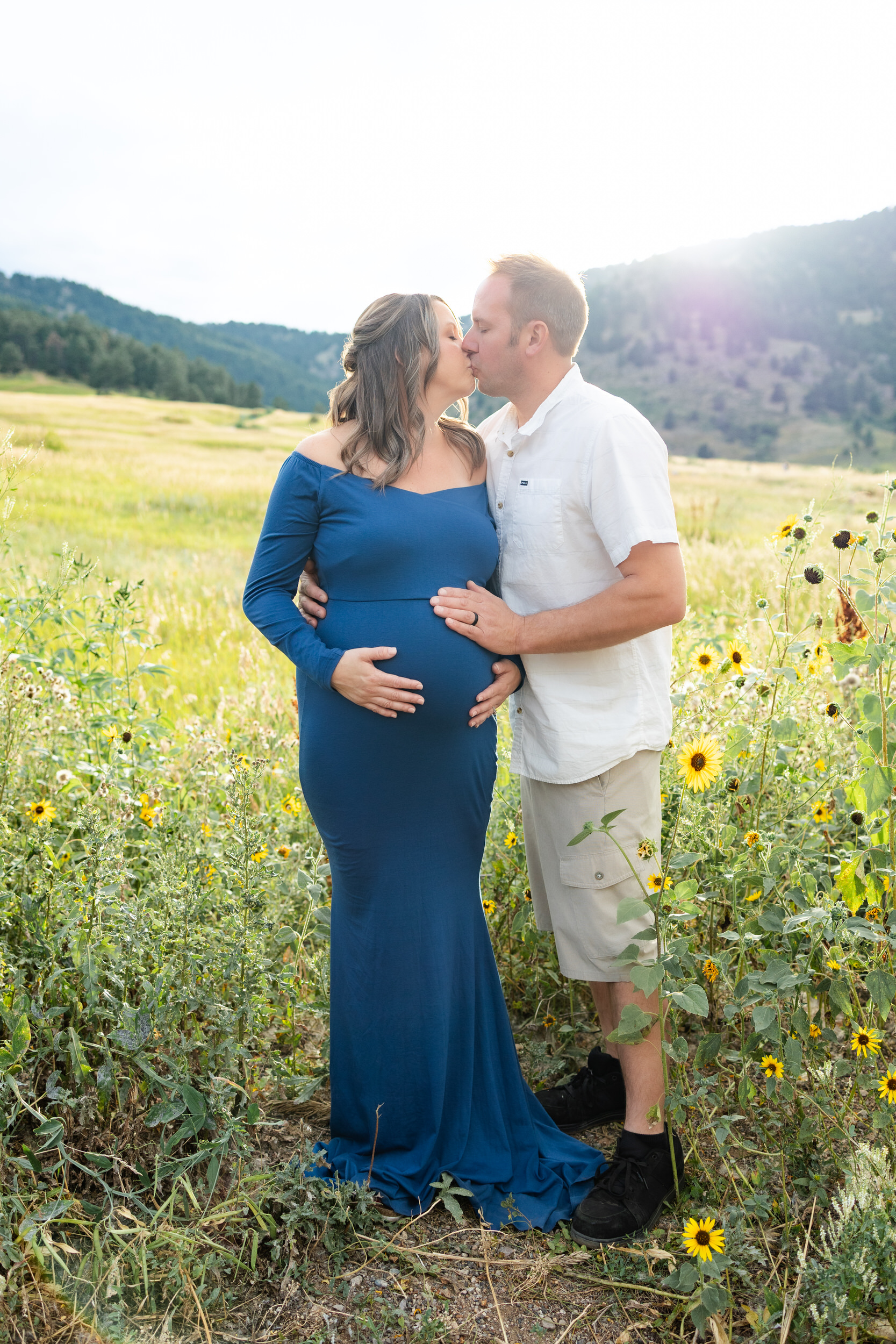 Husband and wife share a kiss while both of them have hands on her pregnant belly.