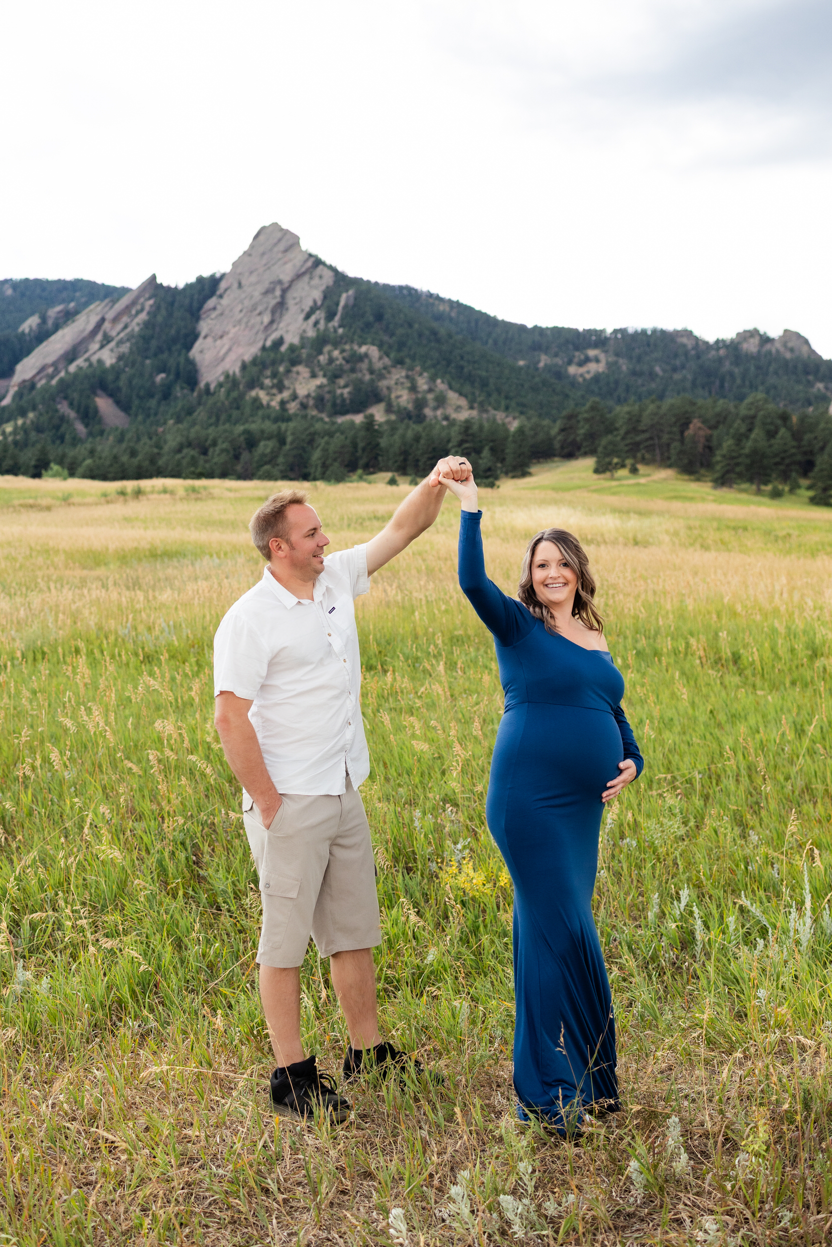 Husband twirls his pregnant wife in a mountain field.