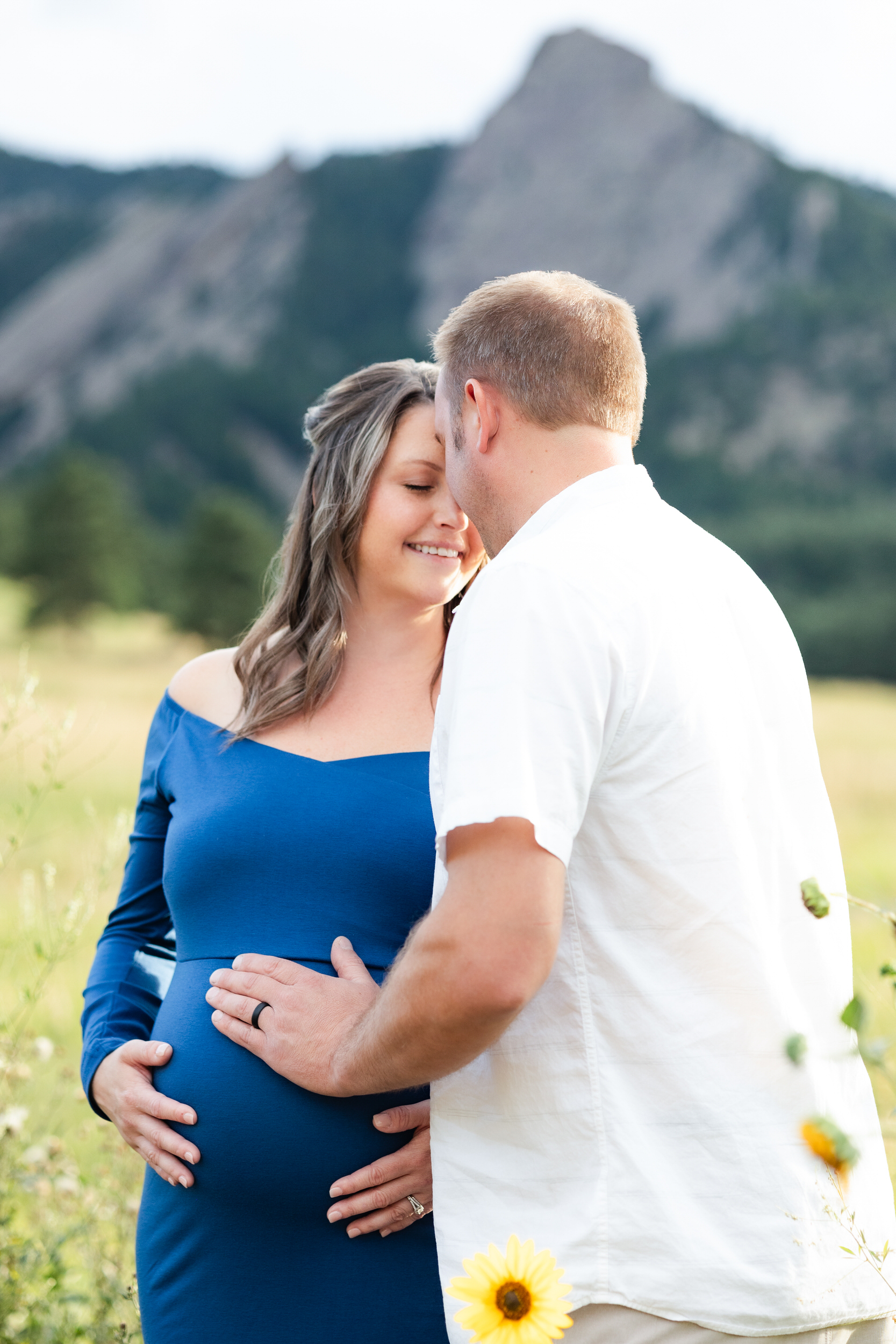 Husband and wife stand forehead to forehead with hands on her pregnant belly.