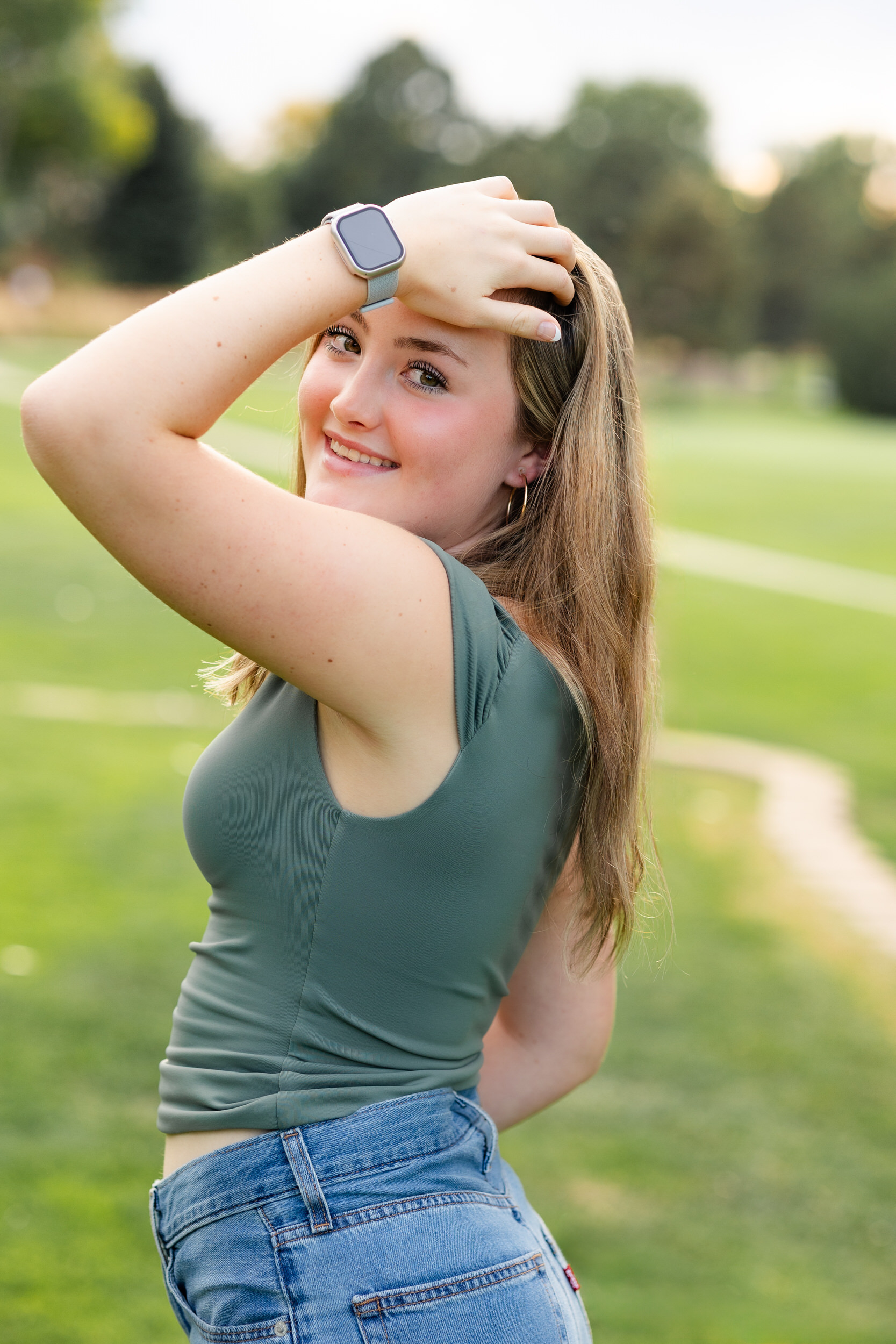 A young woman runs her hand through her hair and smiles at the camera.