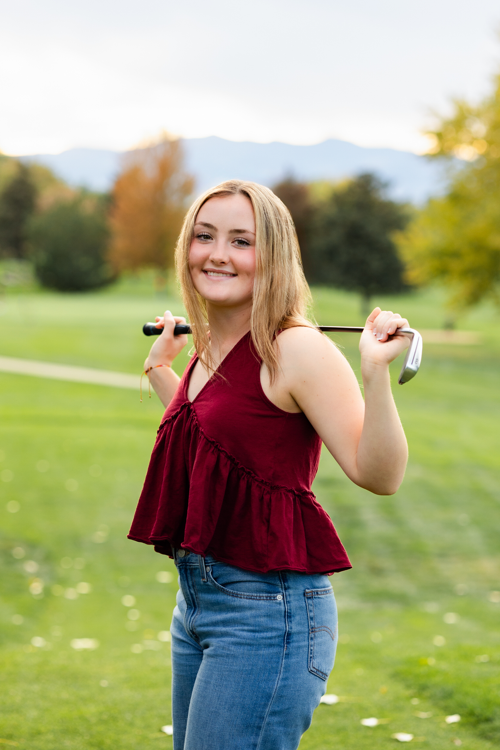 A young woman rests a putter on her shoulders and smiles at the camera.