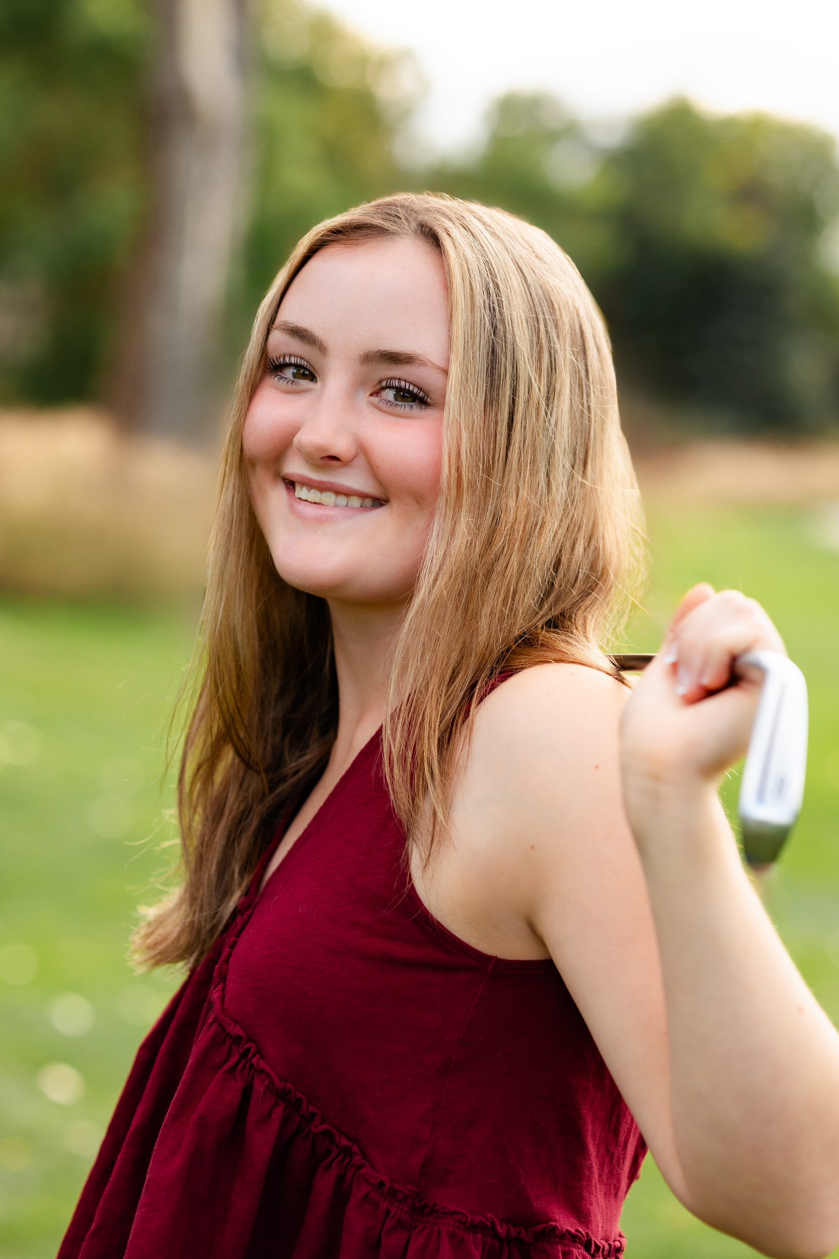 A young woman rests a putter on her shoulders and smiles at the camera.