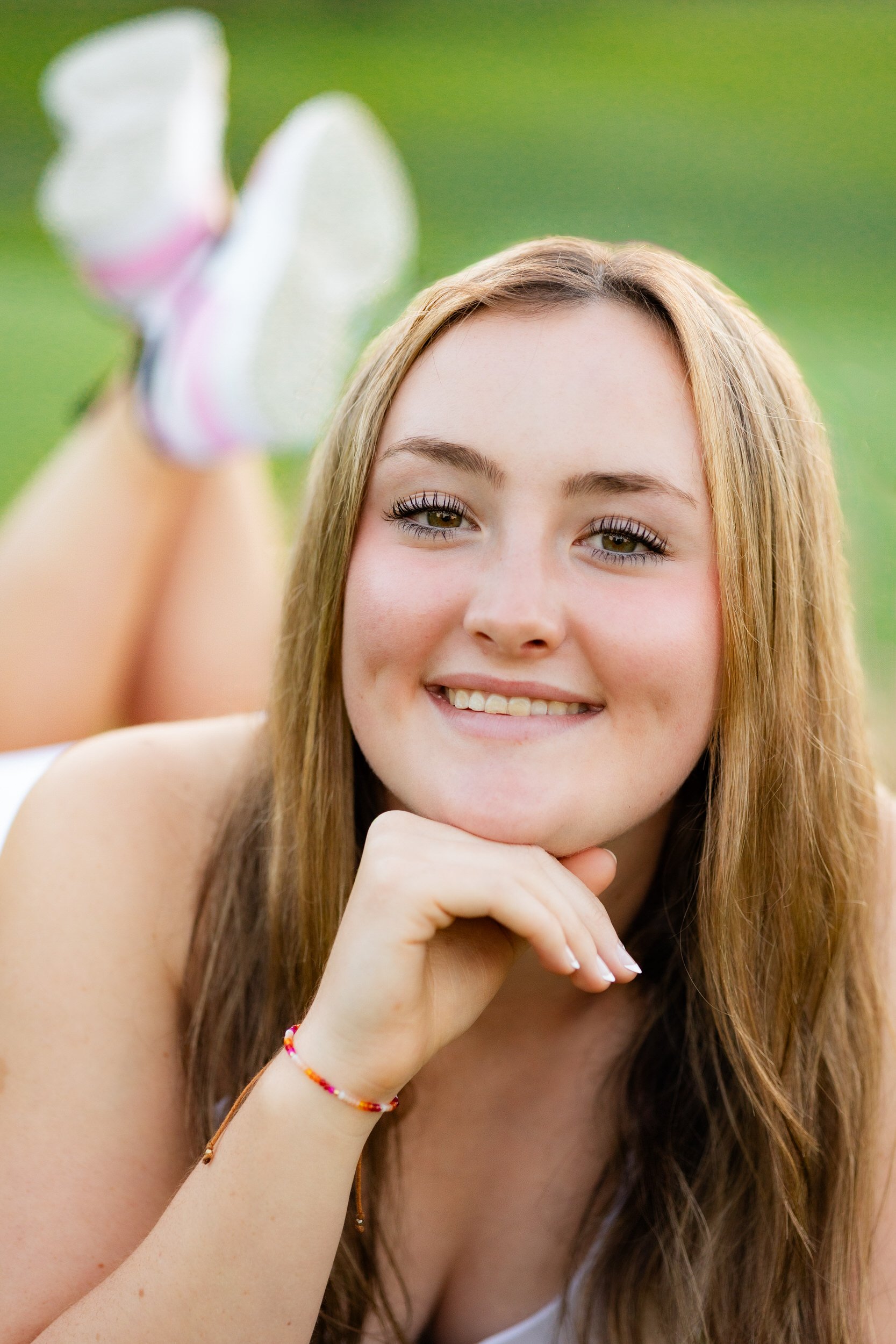 A young woman lying on her belly rests her chin on her hand and smiles at the camera.