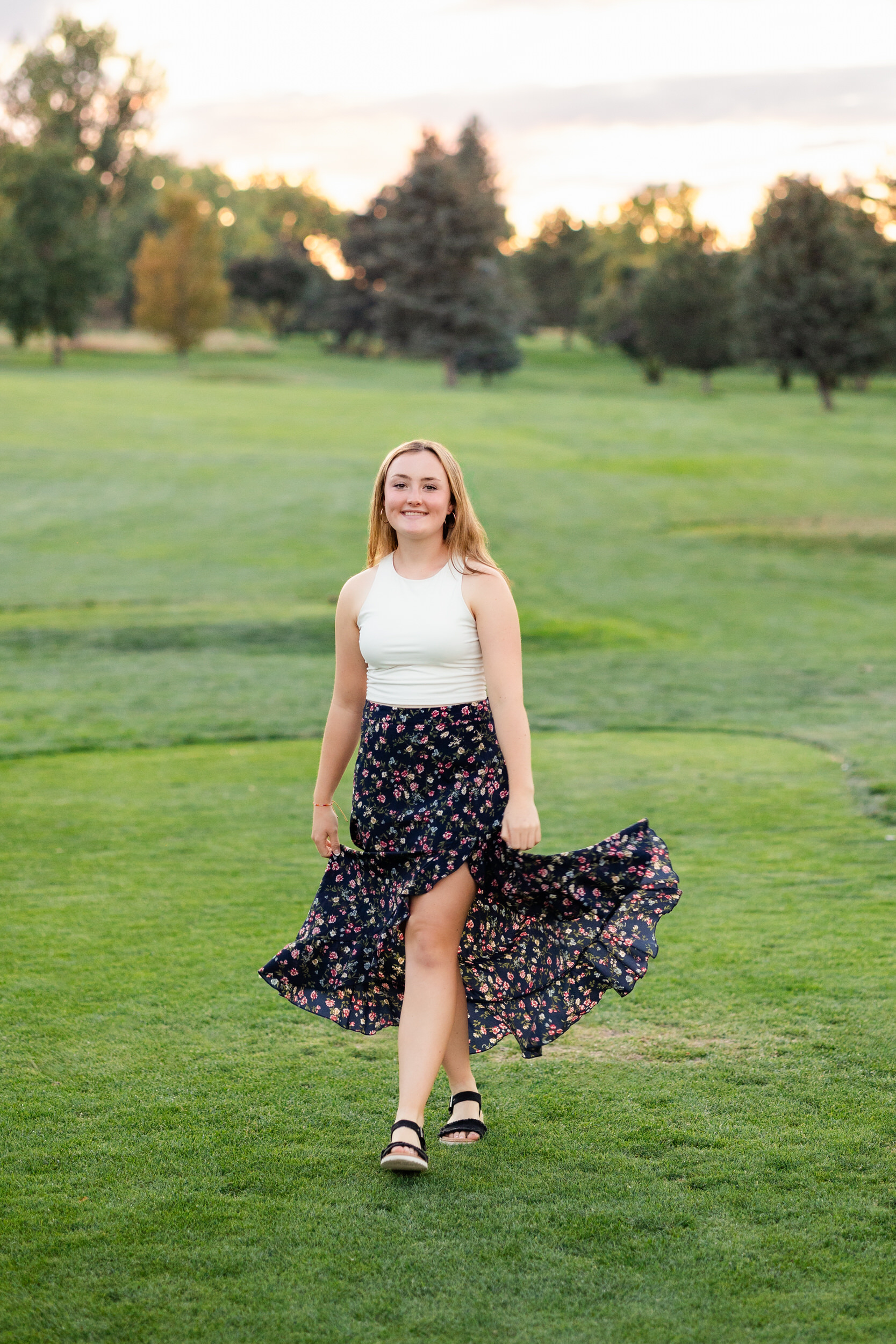 A young woman in a flowy skirt walks on the green at a golf course.
