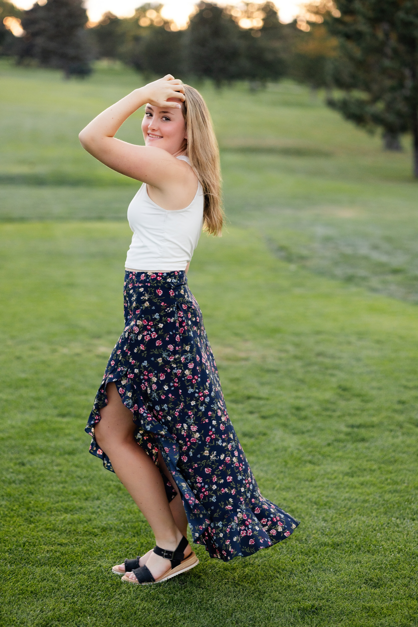 A young woman stands on the green at a golf course and runs her hand through her hair and smiles at the camera.