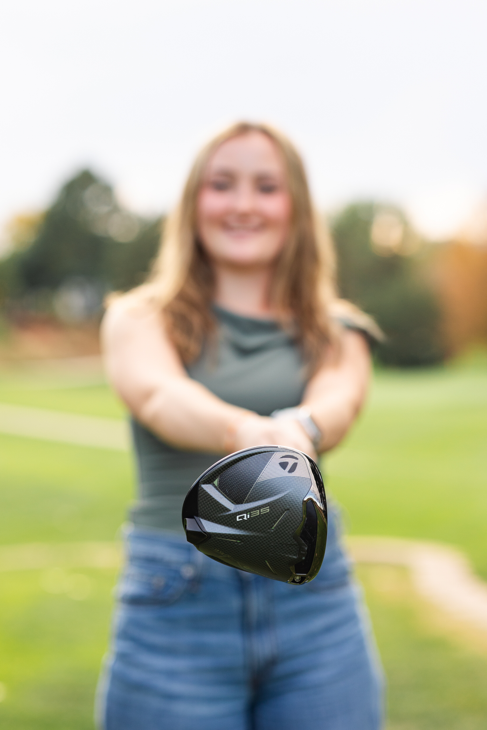Close up shot of a driver and the woman holding the driver is blurred in the background.