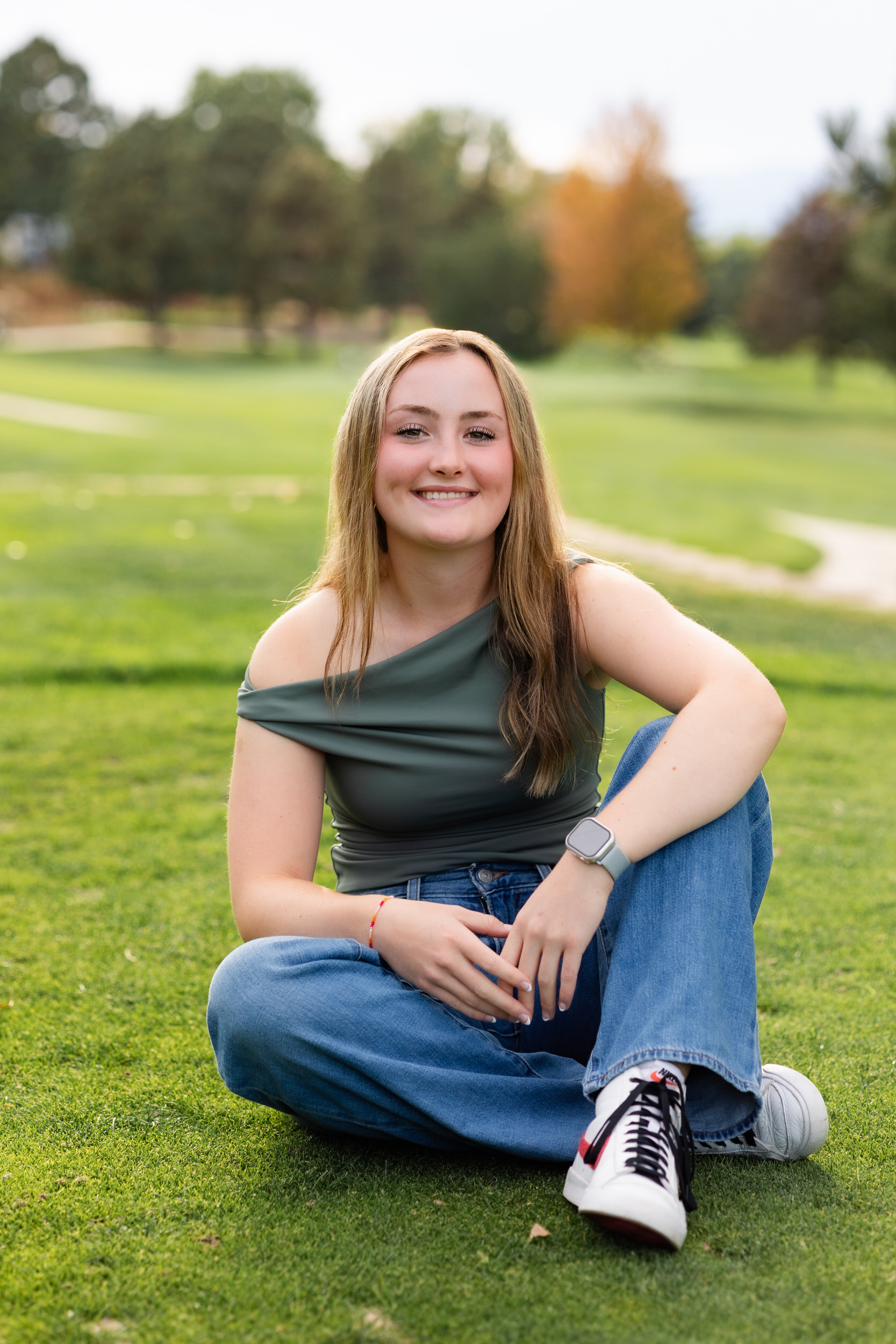 A young woman sits on a golf course and smiles at the camera.