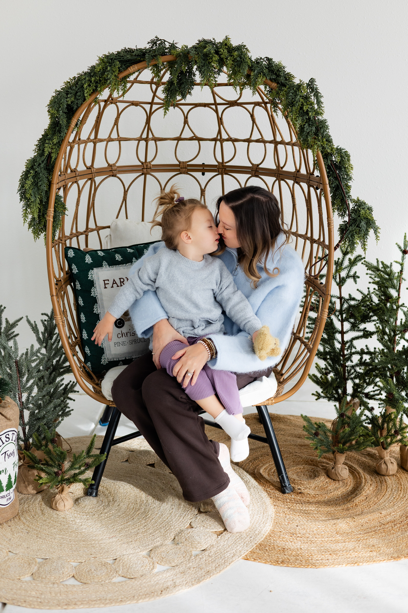 Mom and young daughter sit in egg-style chair and give each other Eskimo kisses.