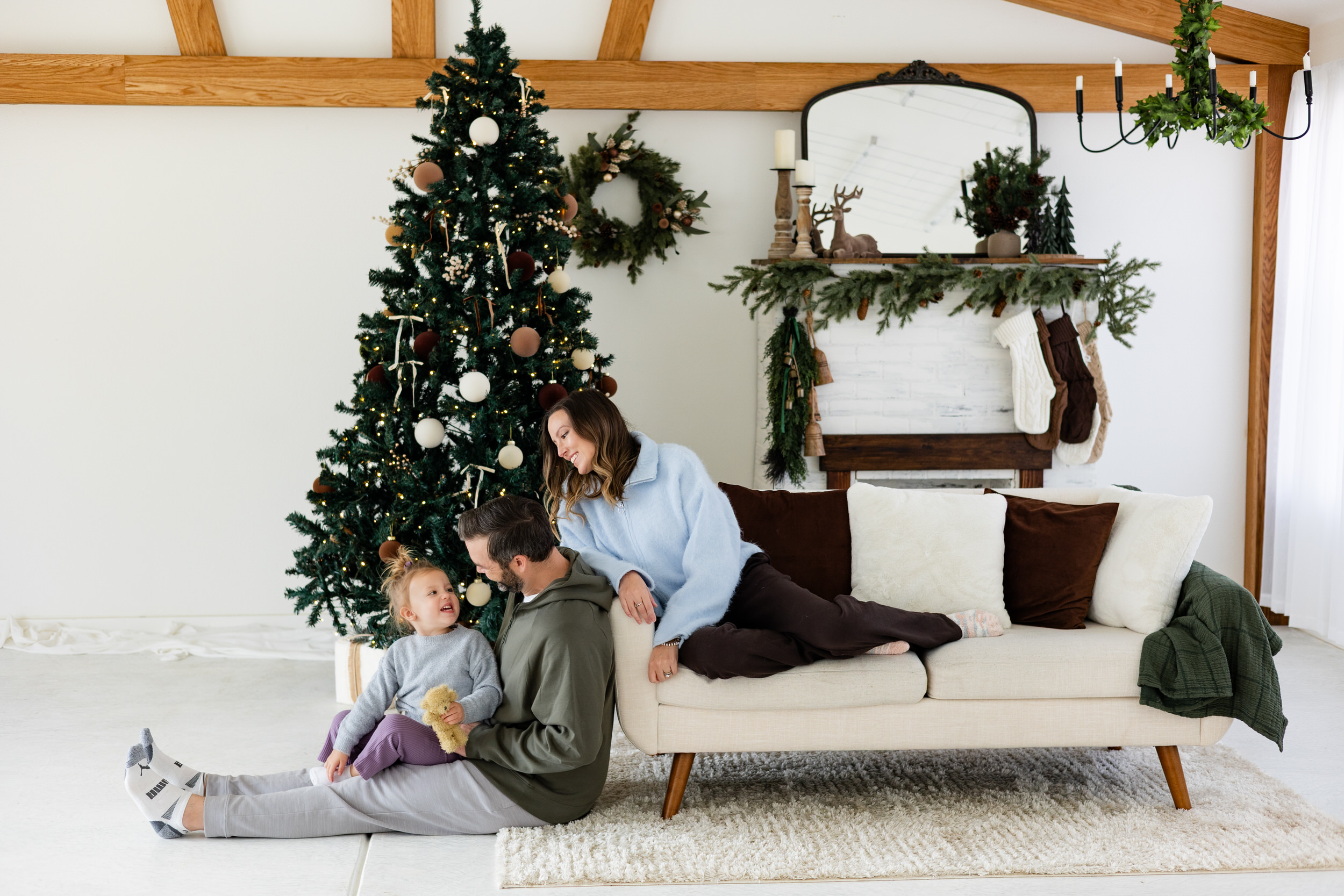 Dad sits on floor with young daughter and mom sits on couch and looks down at them smiling.