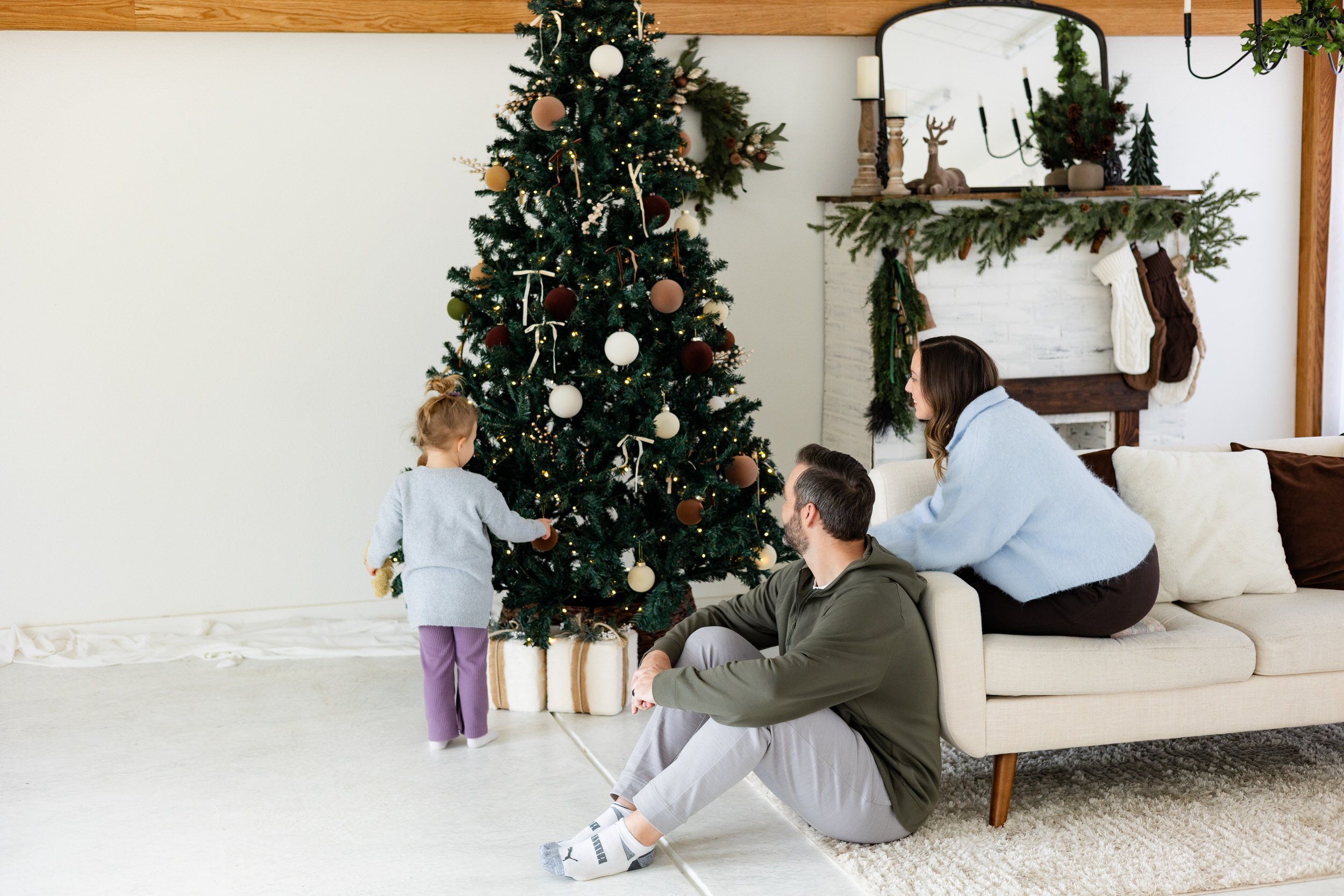 Little girl looks at Christmas tree while mom and dad smile at her.