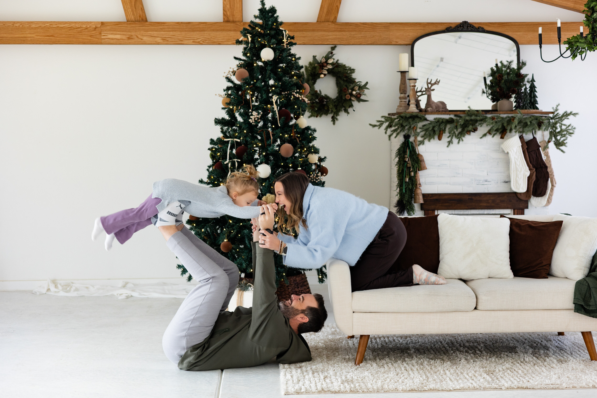 Dad lifts young daughter superman-style while mom smiles at her.