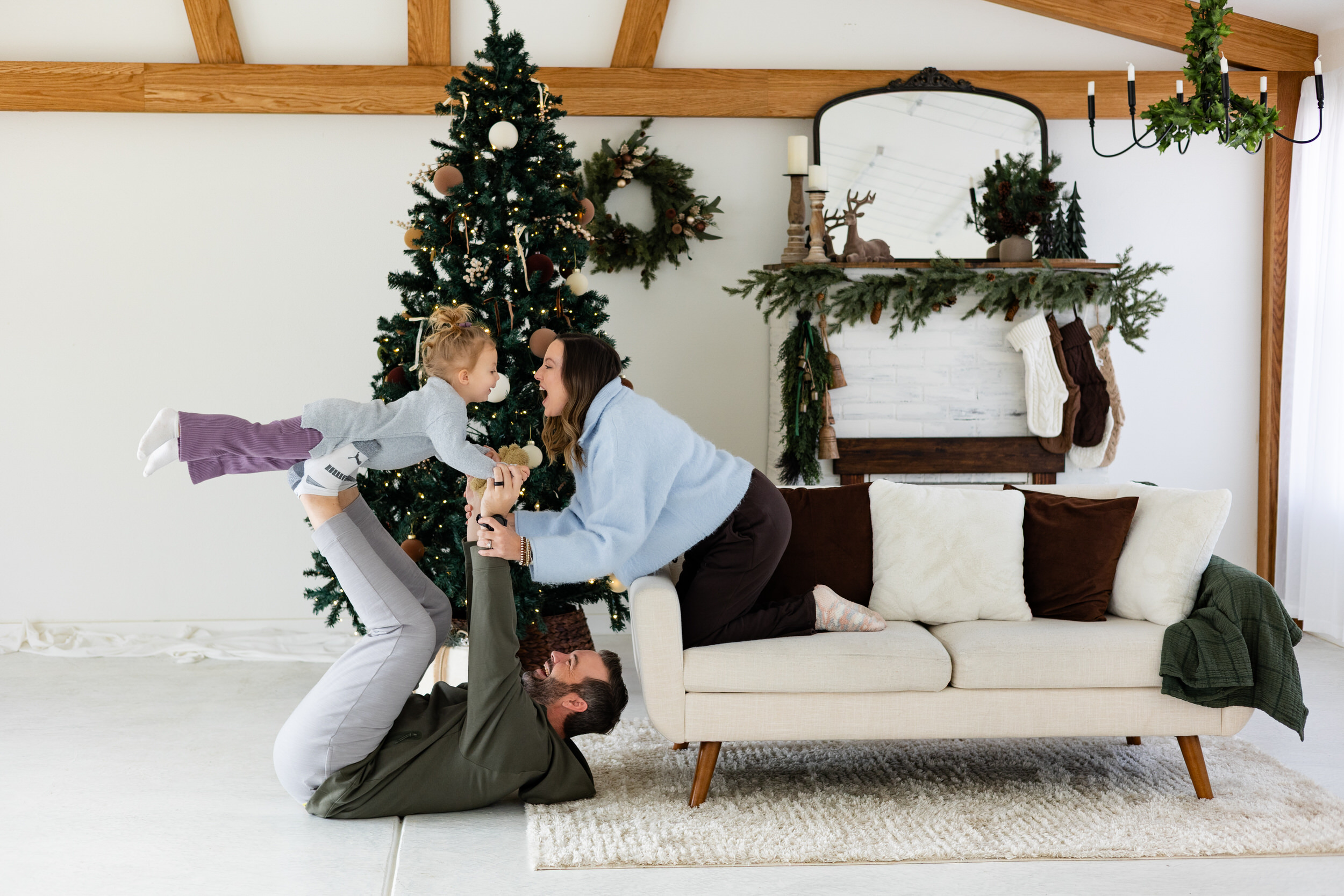 Dad lifts young daughter superman-style while mom smiles at her.