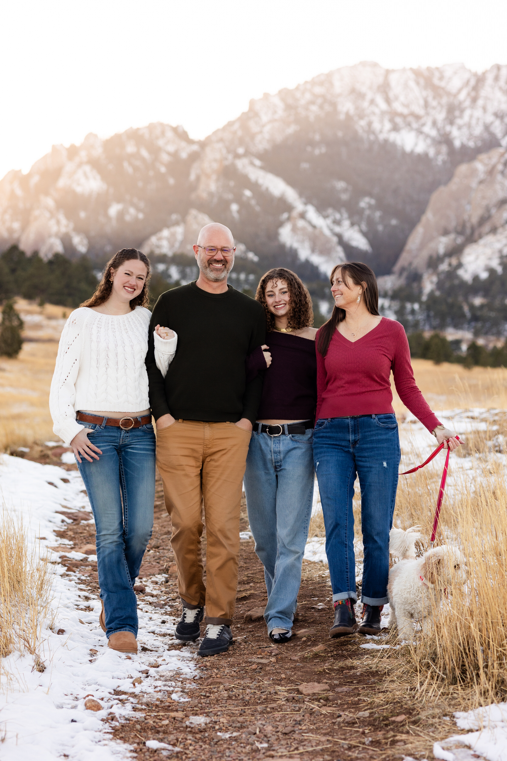 A family of four and their dog walk down a path and smile at each other.