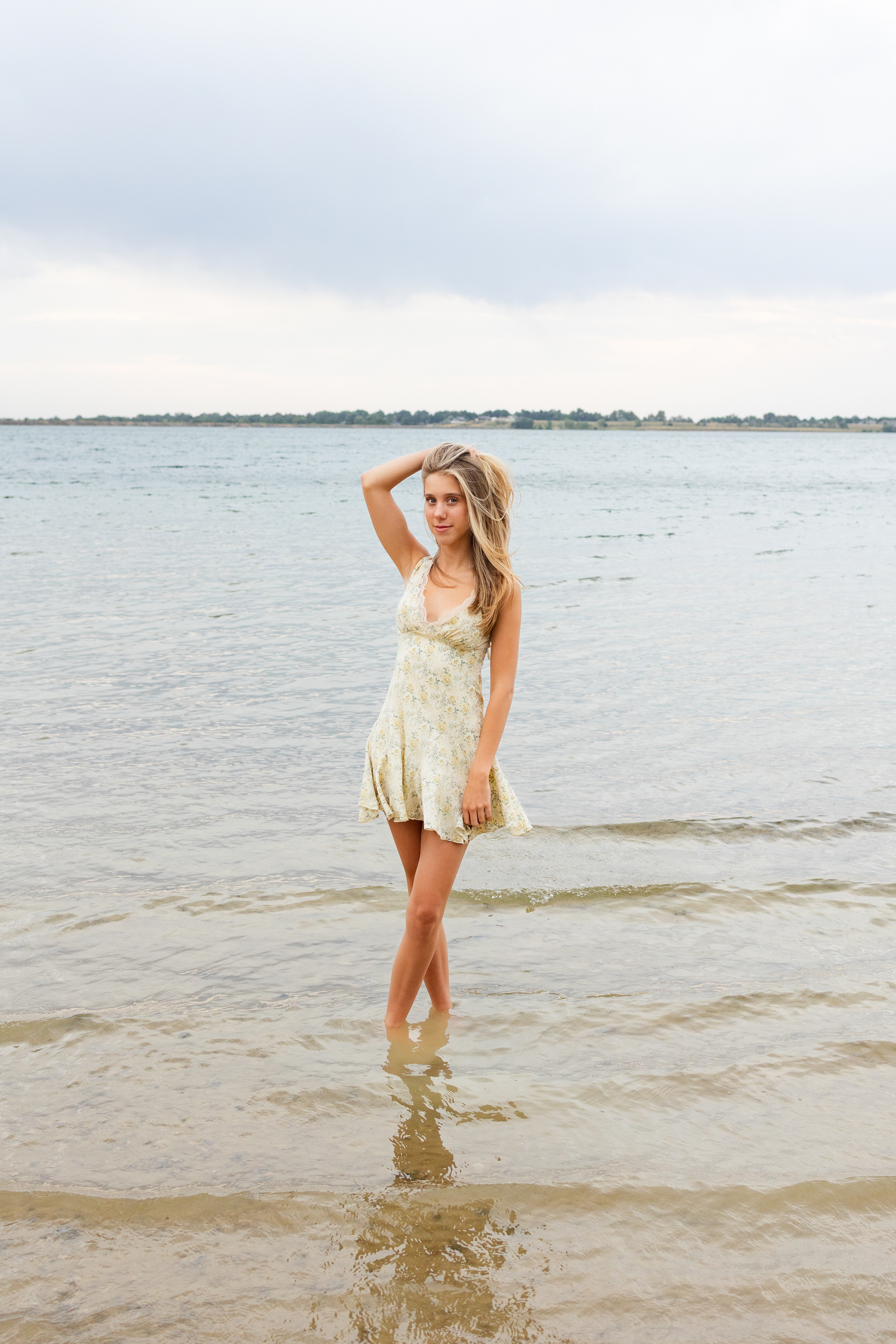 A young woman stands barefoot in a lake and runs her hand through her hair.