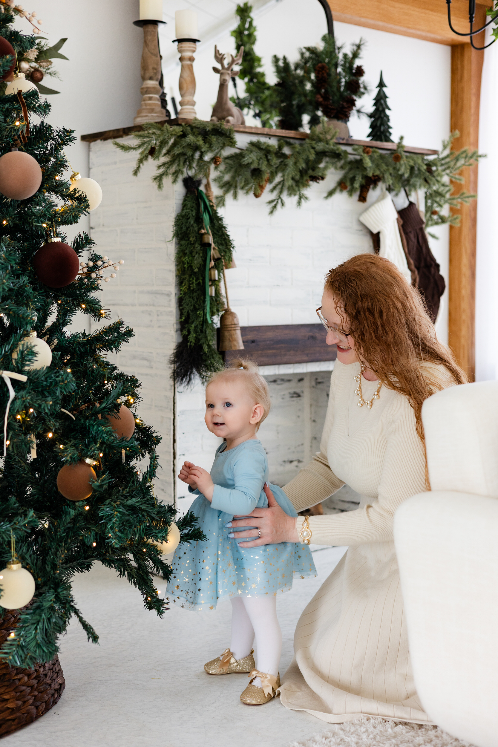 Baby girl looks at Christmas tree while mom holds her.
