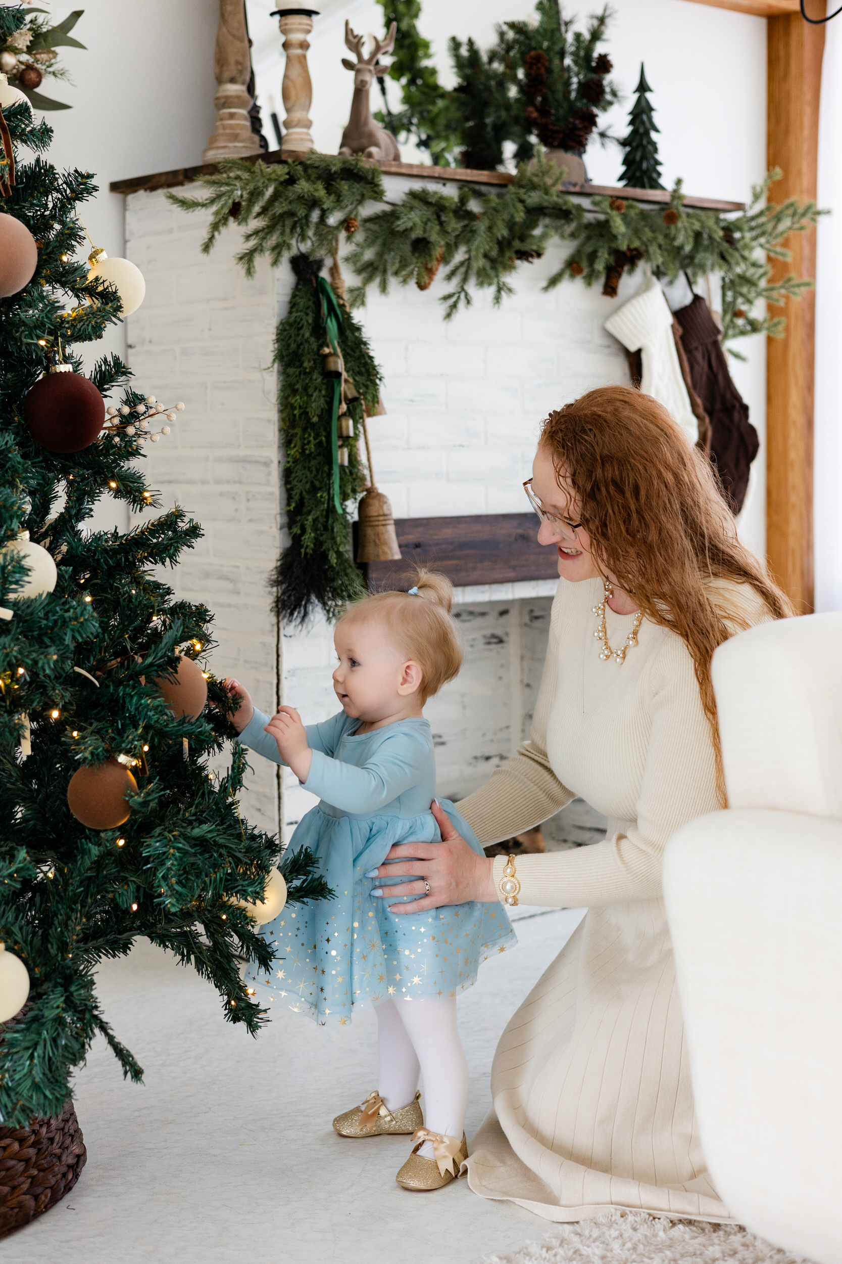 Baby girl looks at Christmas tree while mom holds her.