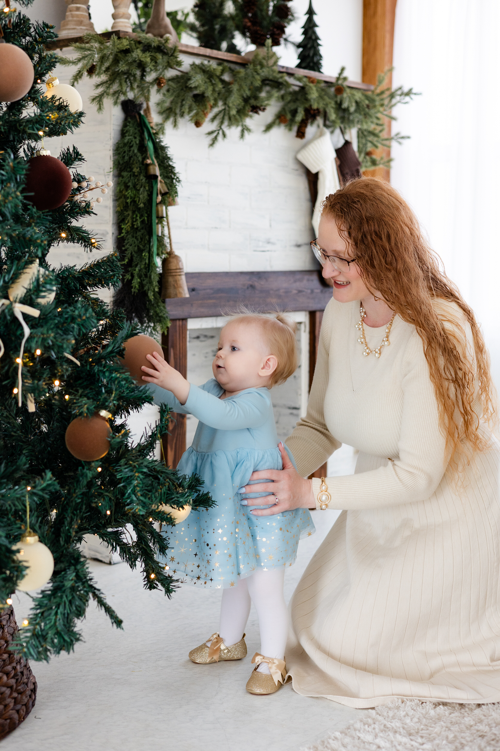 Baby girl looks at Christmas tree while mom holds her.