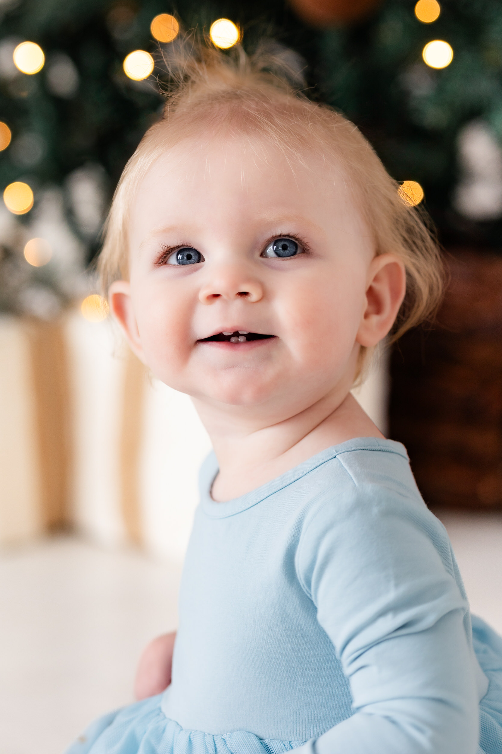 Baby girl sits in front of Christmas tree.