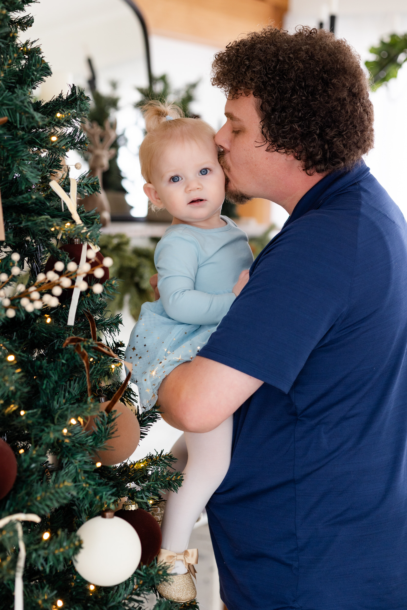 Dad holds baby girl and kisses her cheek.