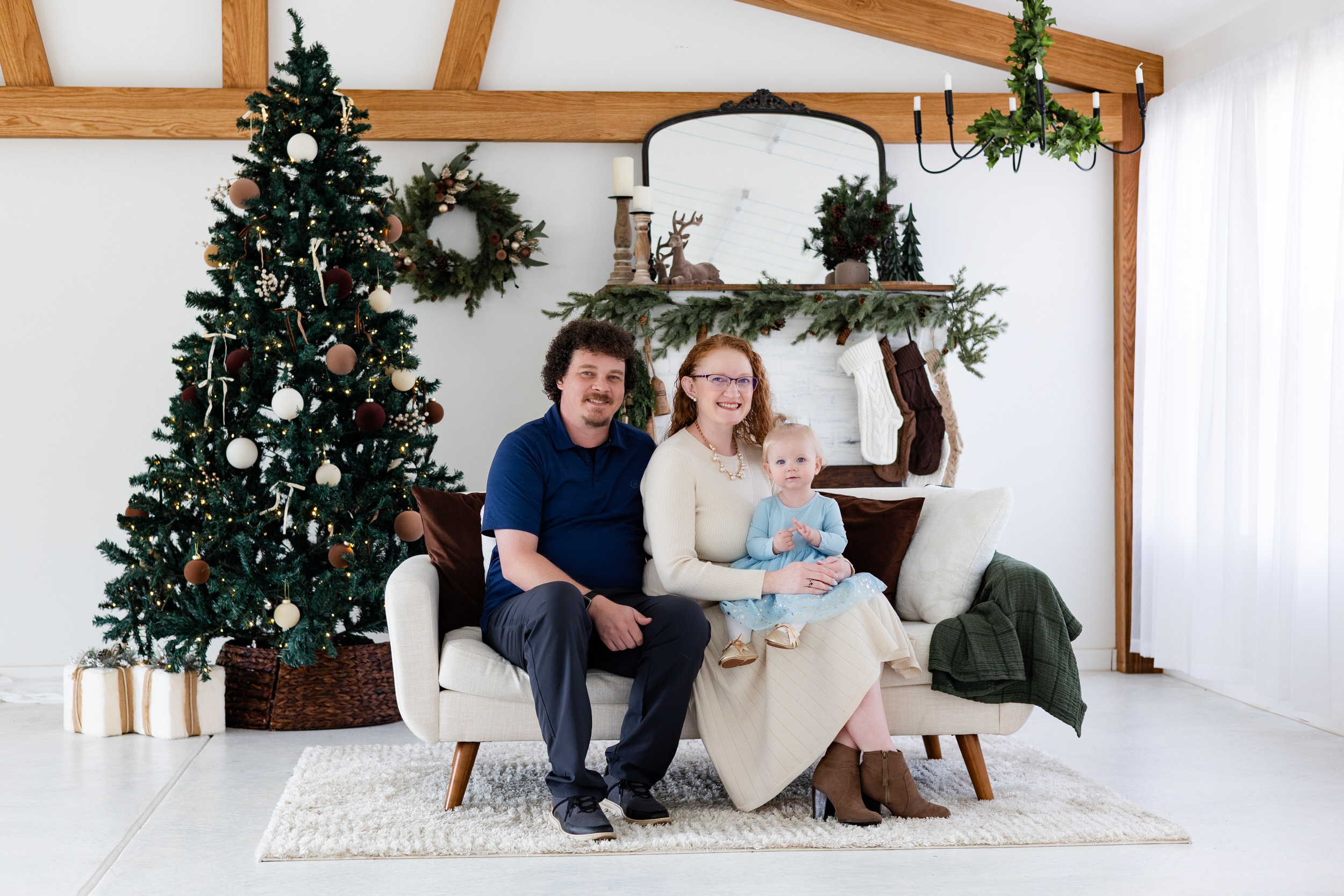 Mom and dad sit on a white couch with baby girl sitting on mom's lap.