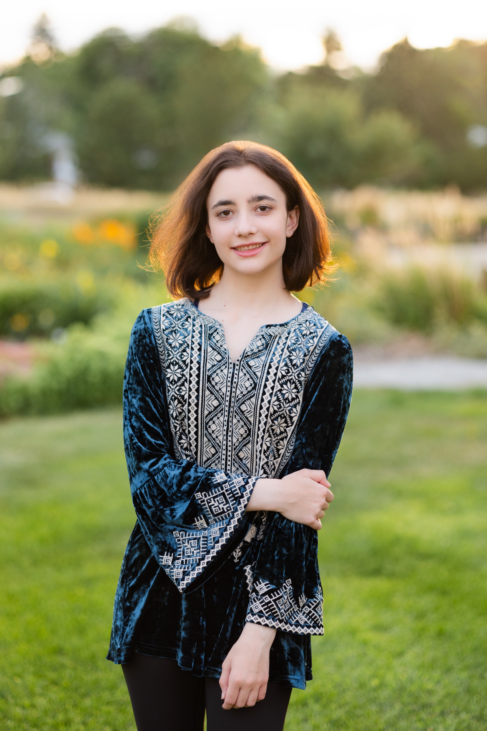 A young woman stands in a garden and smiles at the camera.