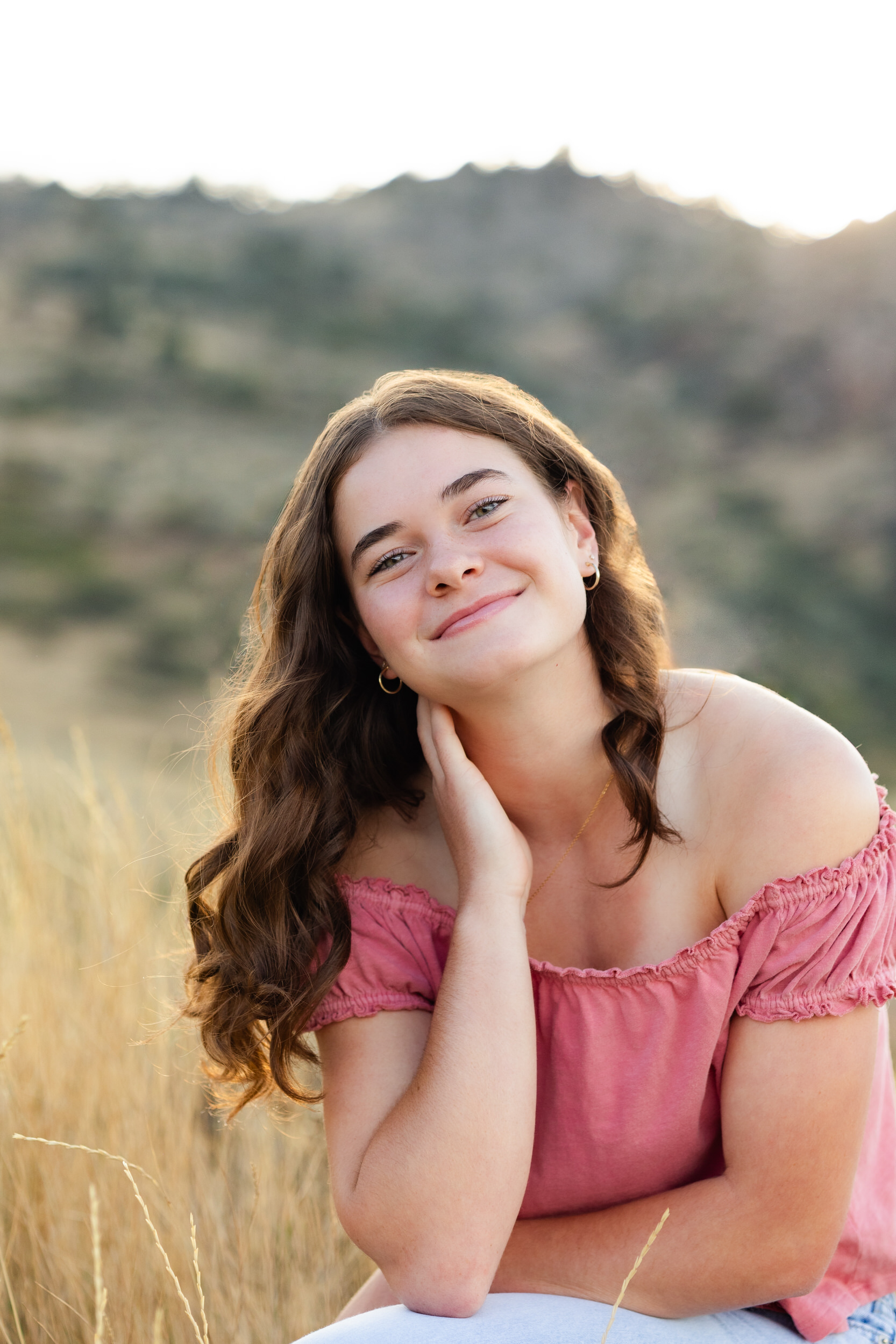 A young woman rests her head on her hand and smiles at the camera.