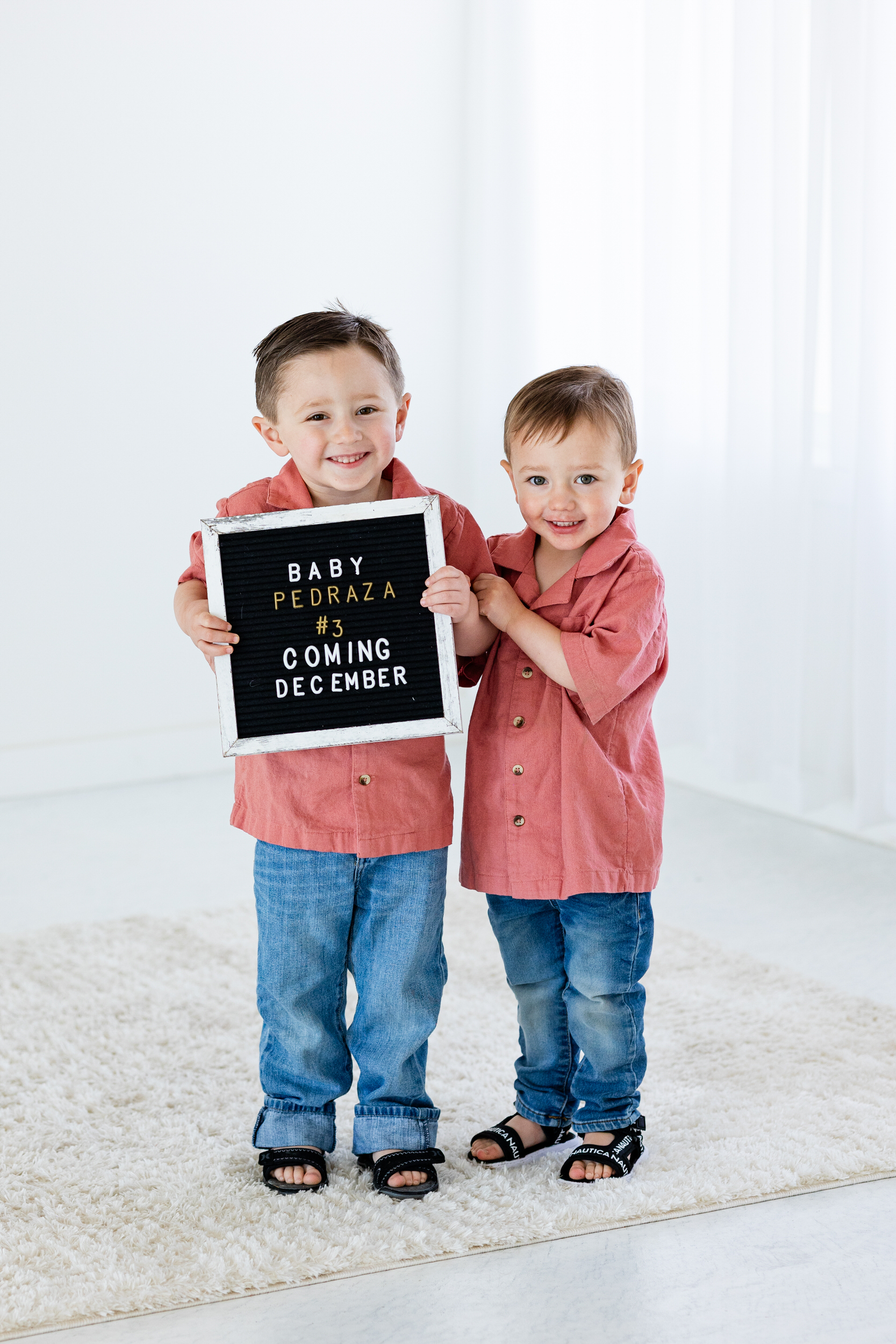 Two little boys hold a sign that reads, "Baby Pedraza #3 coming December".