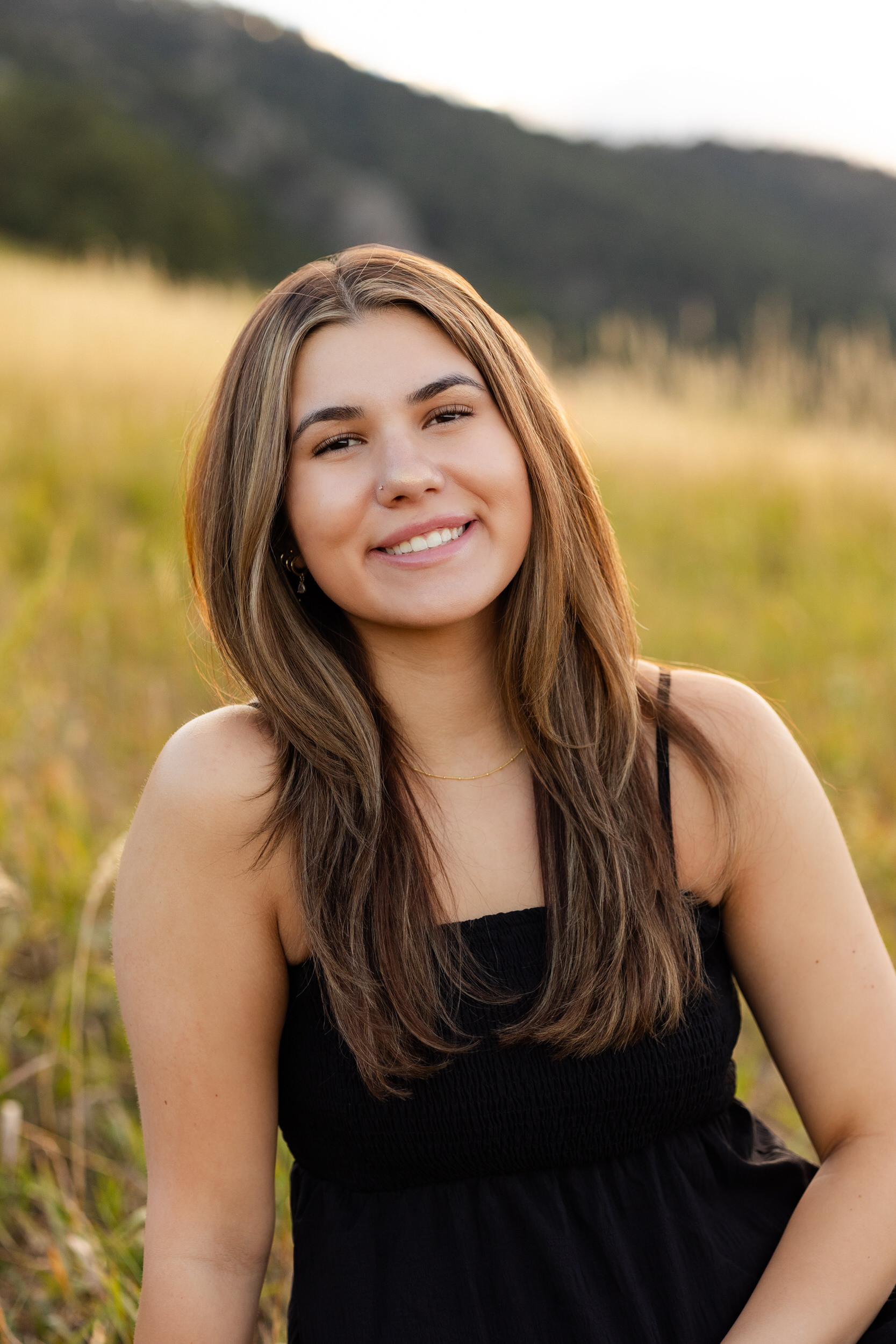 A young woman sits in a field and smiles at the camera.