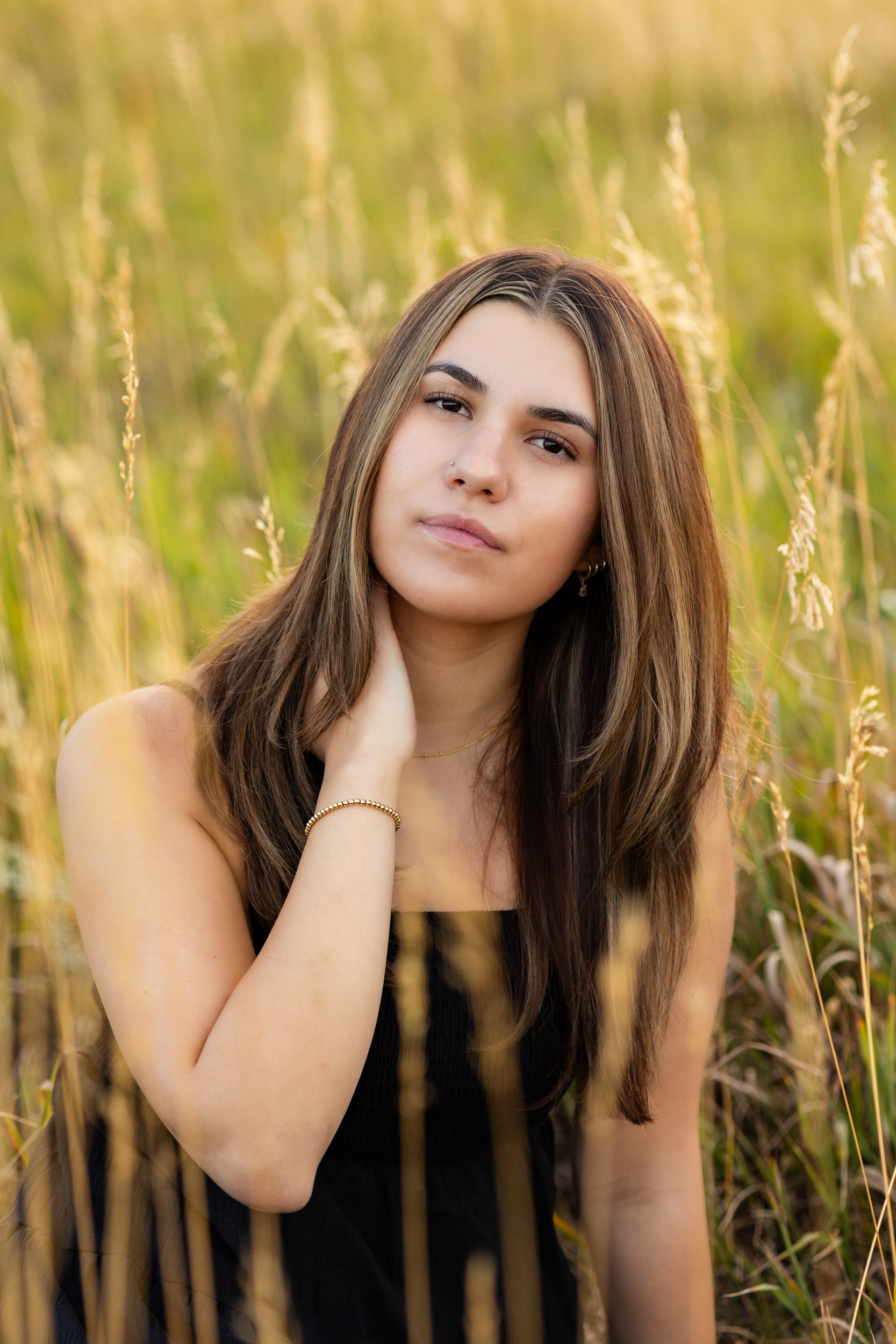 A young woman sits in a mountain field and looks at the camera.