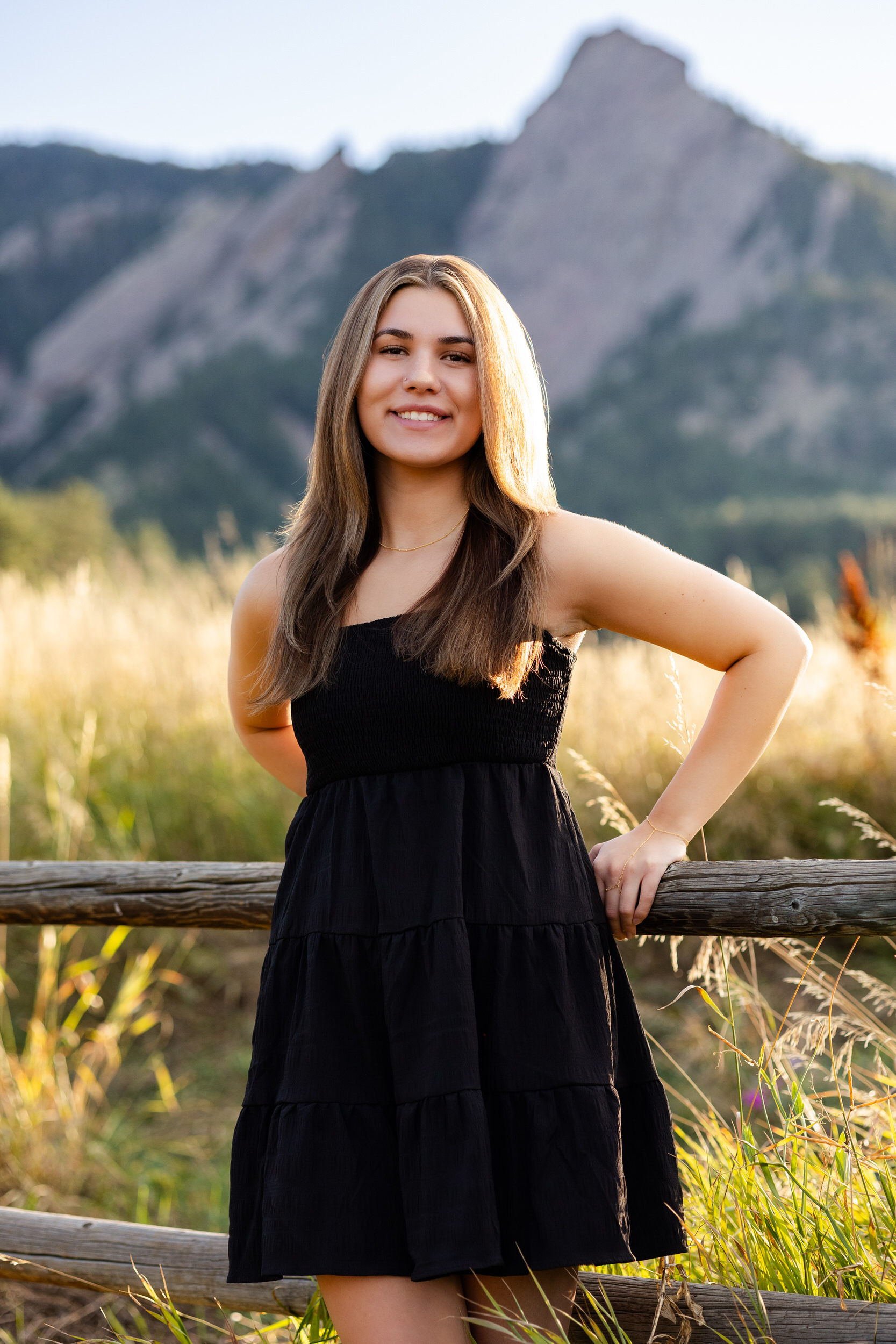 A young woman leans against a fence in Chautauqua Park in Boulder, Colorado and smiles at the camera.