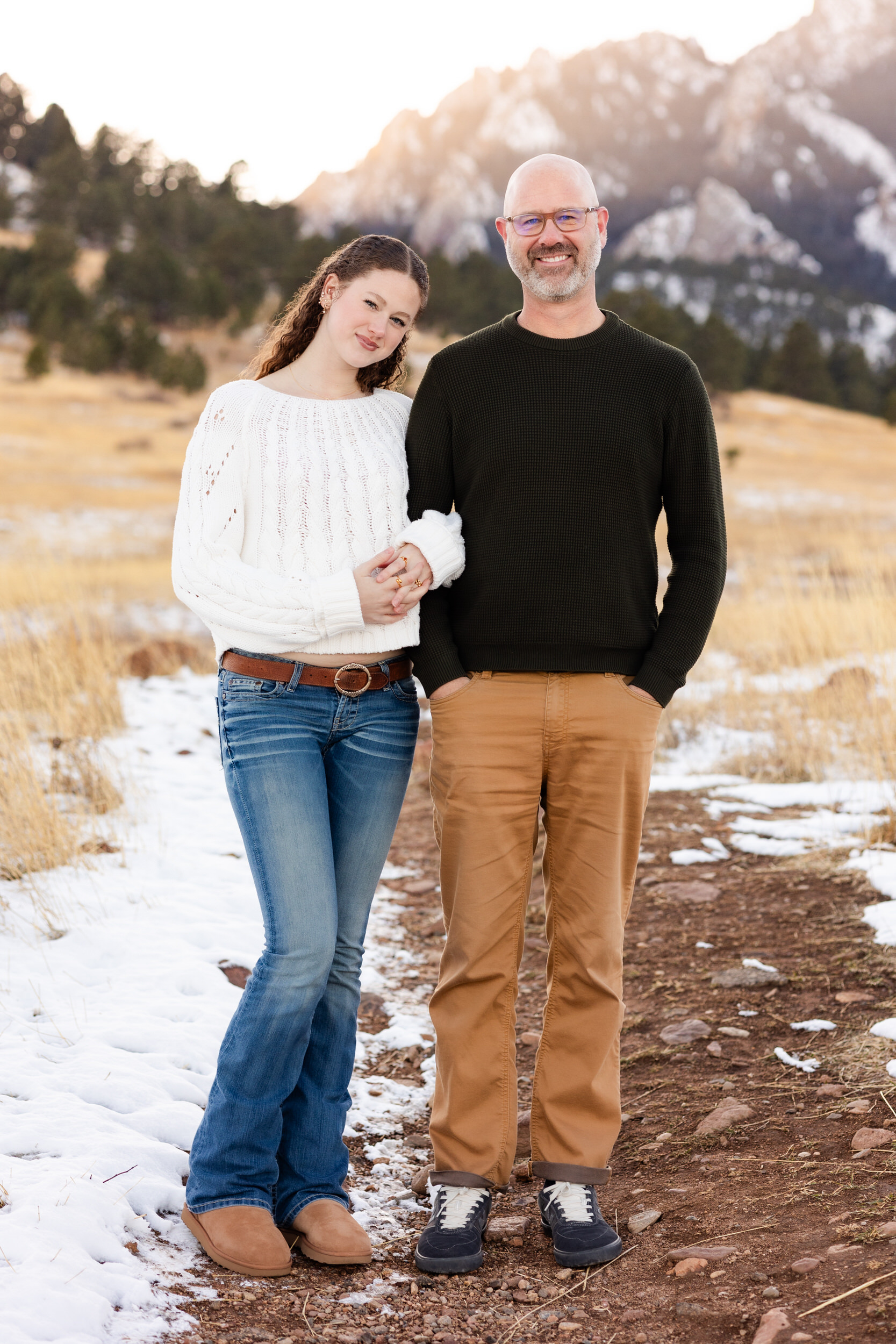 A young woman stands arm-in-arm with her dad and they smile at the camera.
