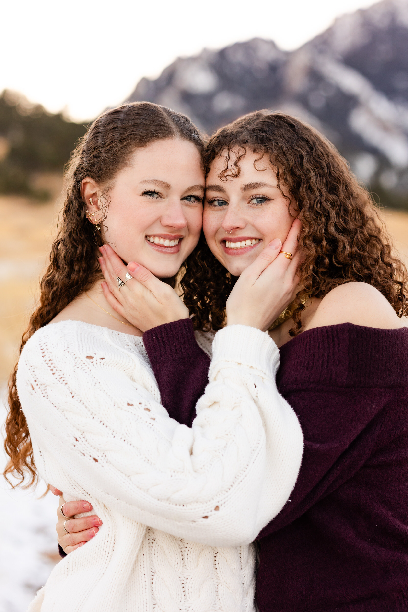 Two sisters hug each other and smile at the camera.
