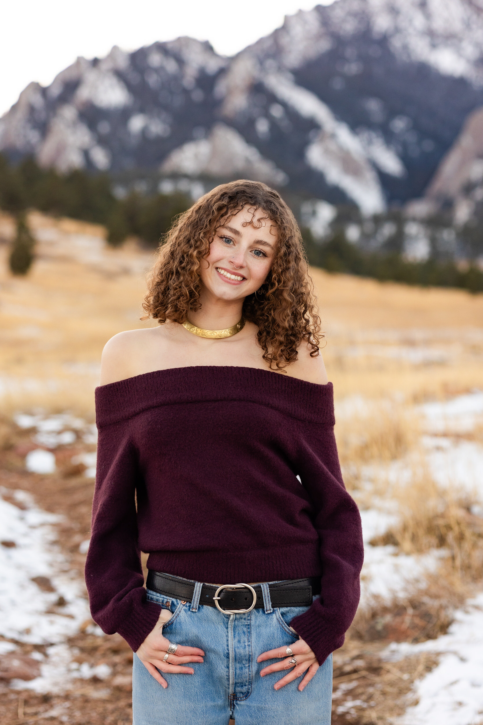 A young woman with hands in pockets smiles at the camera.
