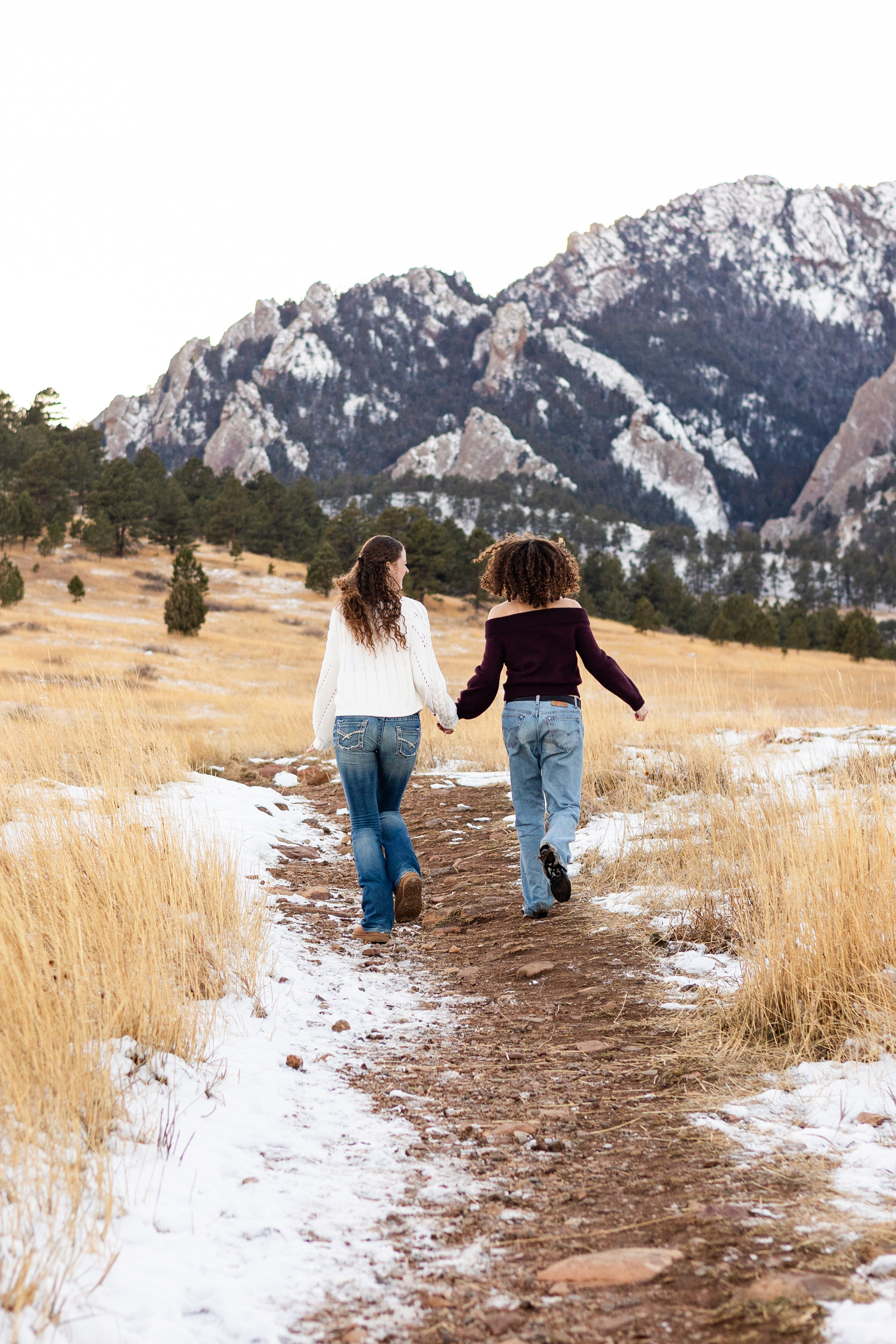 Two young adult sisters hold hands and run down a dirt path.