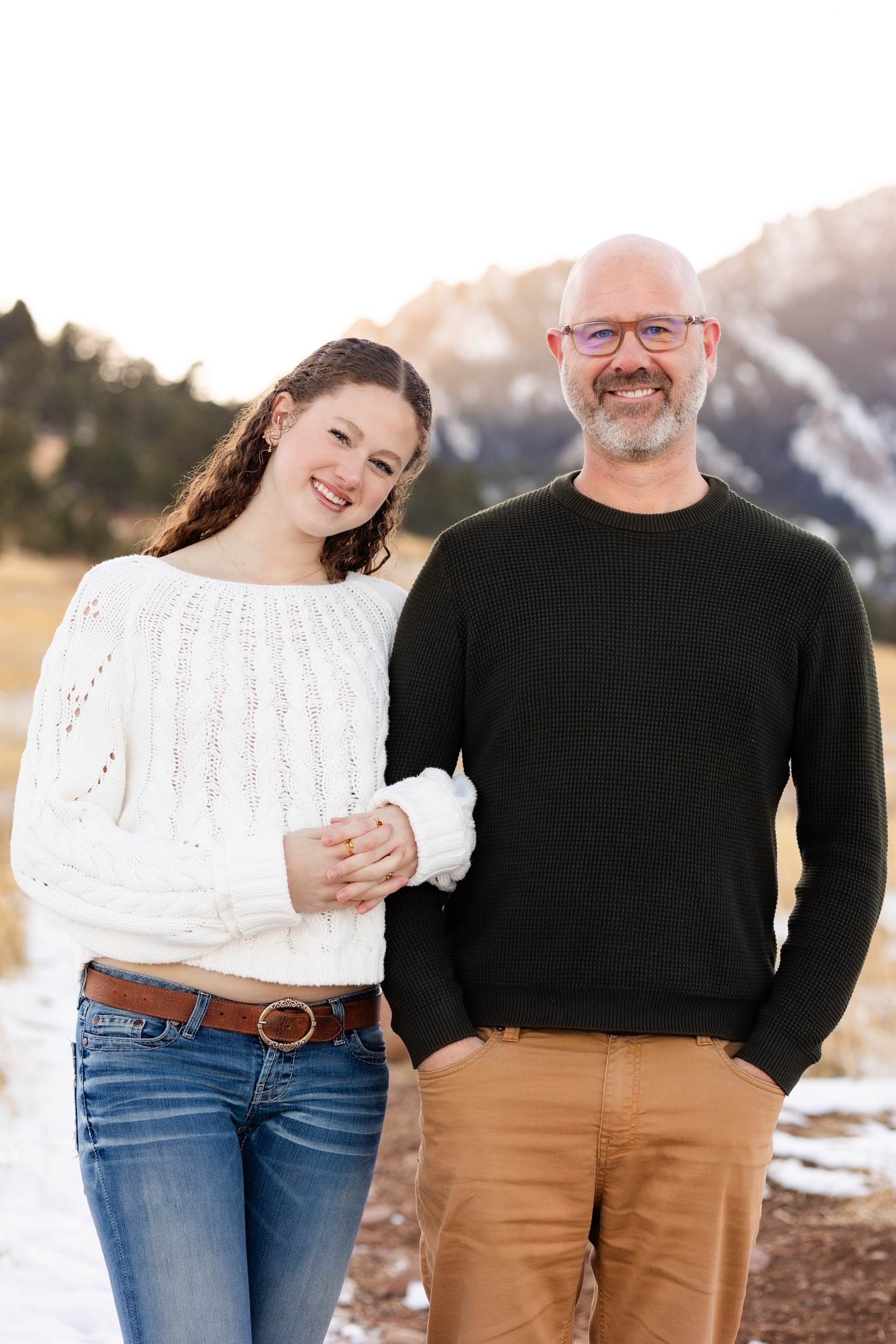 A young woman stands arm-in-arm with her dad and they smile at the camera.