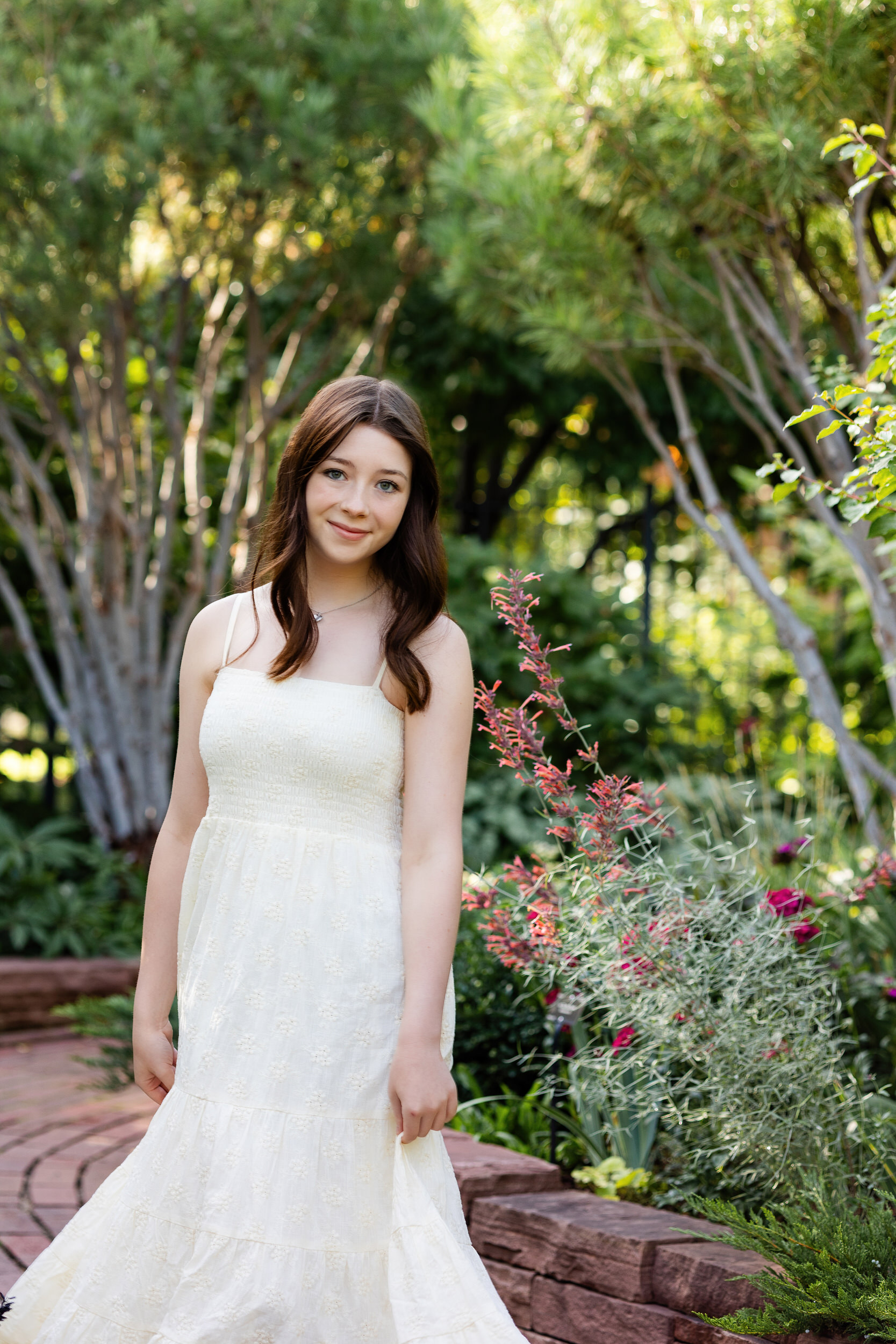 A young woman in a long white dress swishes her skirt as she walks down a path at the Denver Botanic Gardens.