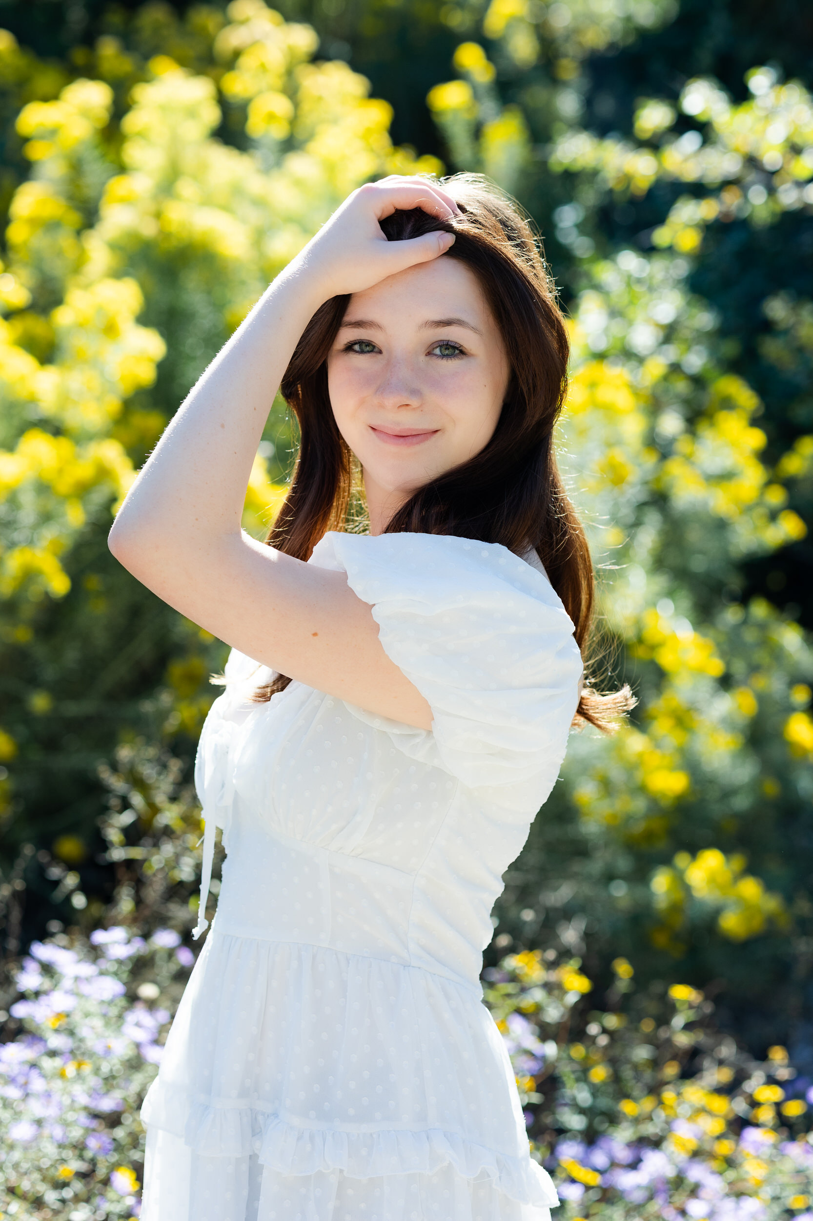A young woman runs one hand through her hair and smiles at the camera while standing in the Denver Botanic Gardens.