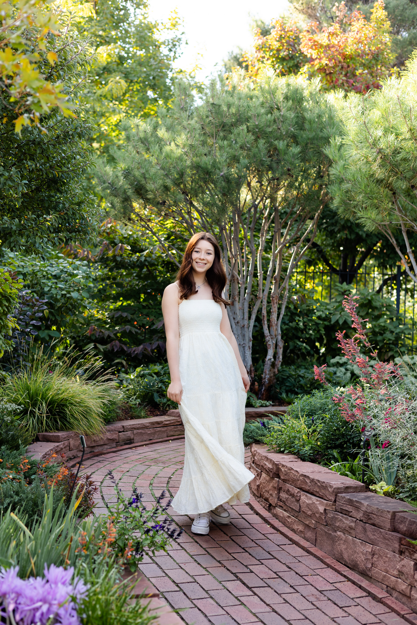 A young woman in a long white dress walks down a garden path at the Denver Botanic Gardens.