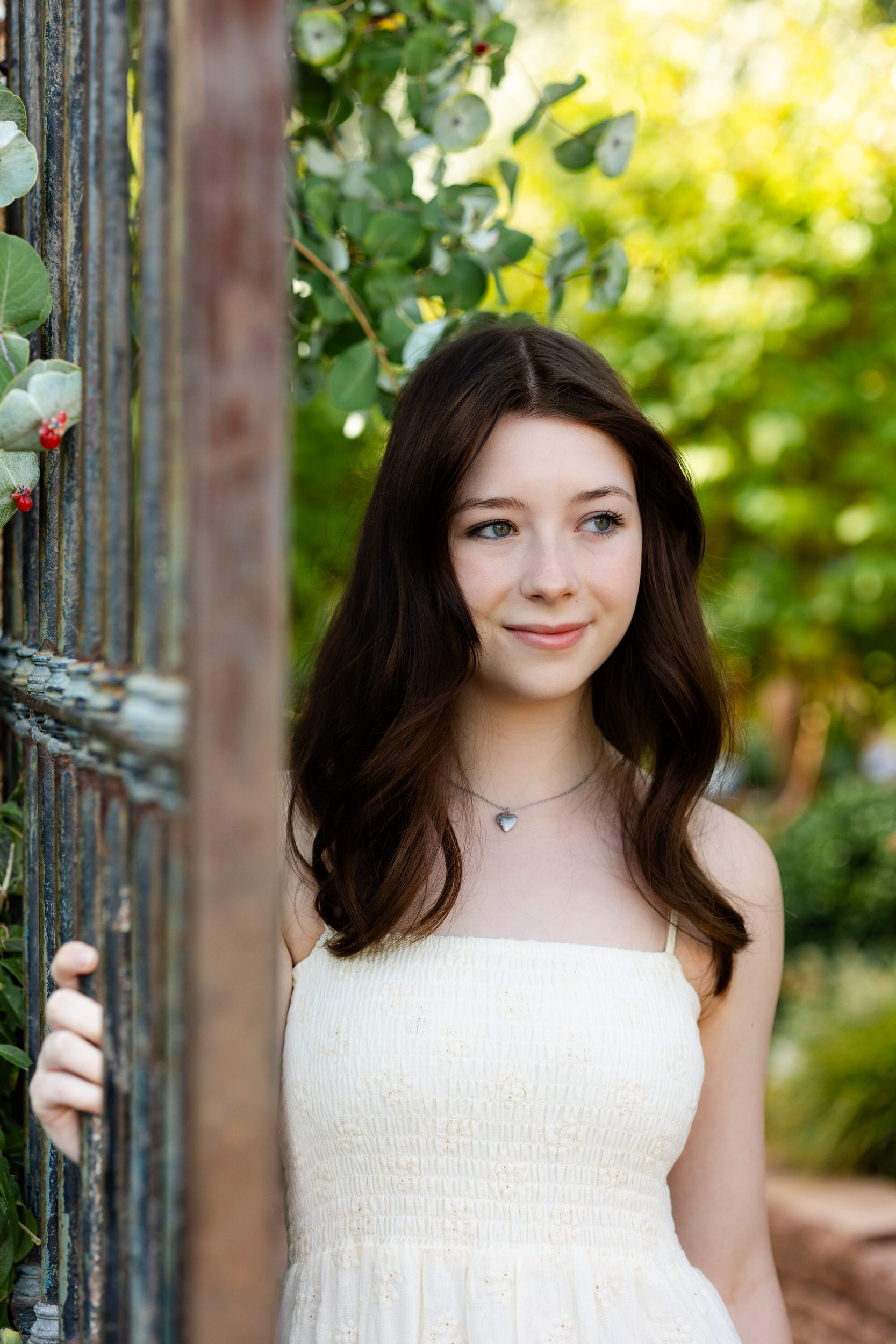 A young woman holds onto a garden gate with one hand and looks off-camera.