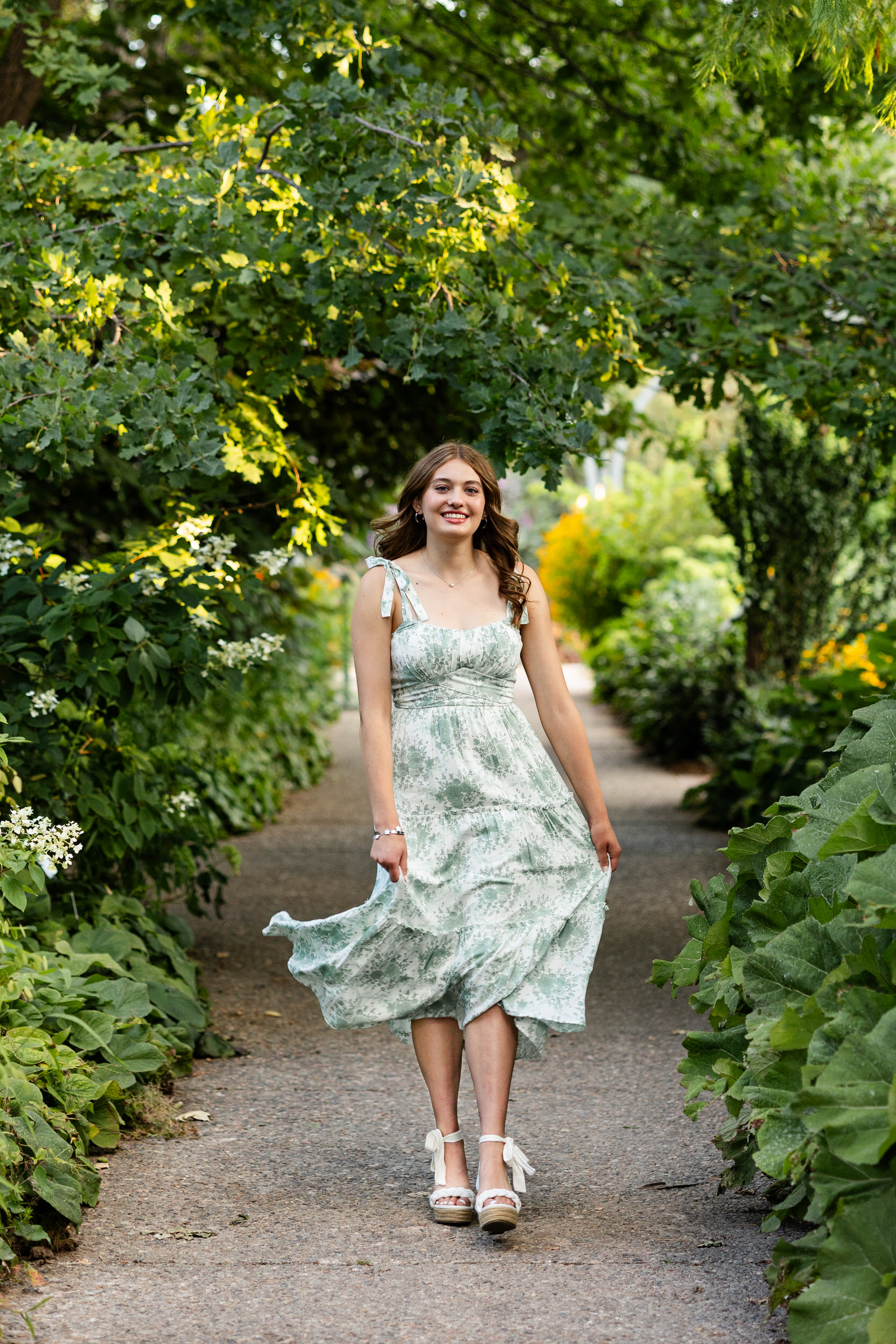 A young woman in a white and green dress walks through a garden.
