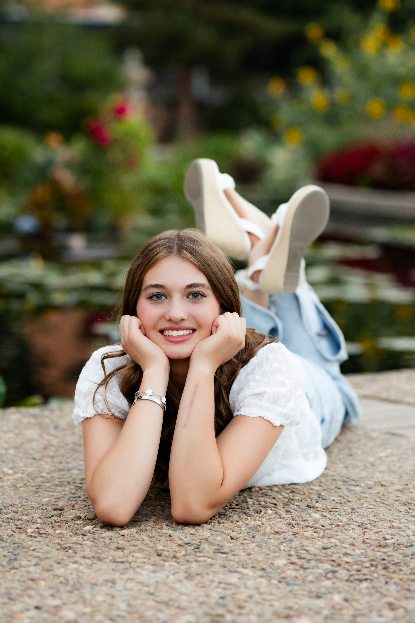 A young woman lays on her belly with her chin propped in her hands and smiles at the camera.