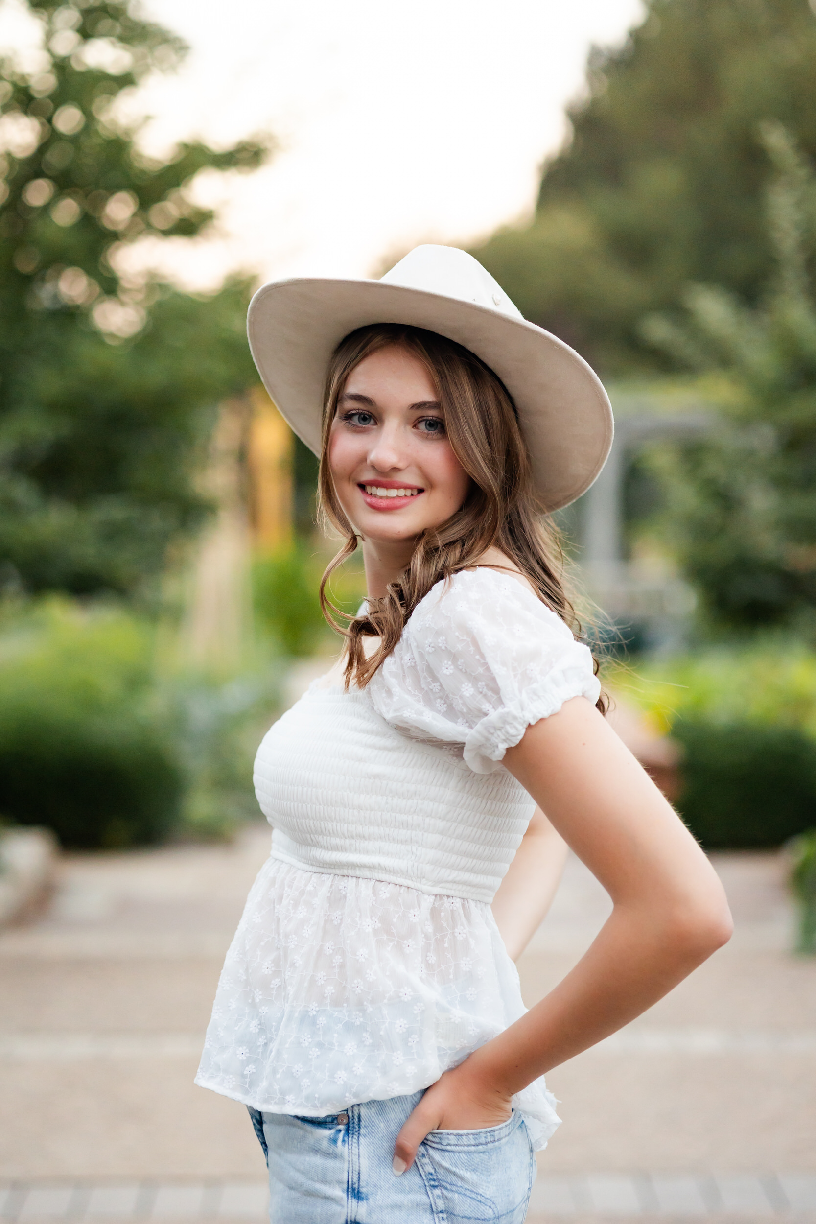 A young woman in a wide-brimmed hat smiles at the camera.